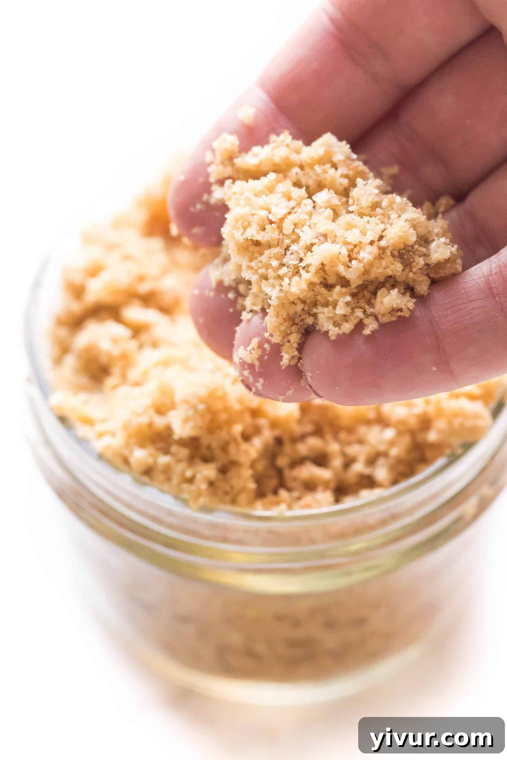 Close-up of crushed pork panko being held above a mason jar, showing the golden, crispy breadcrumb texture.