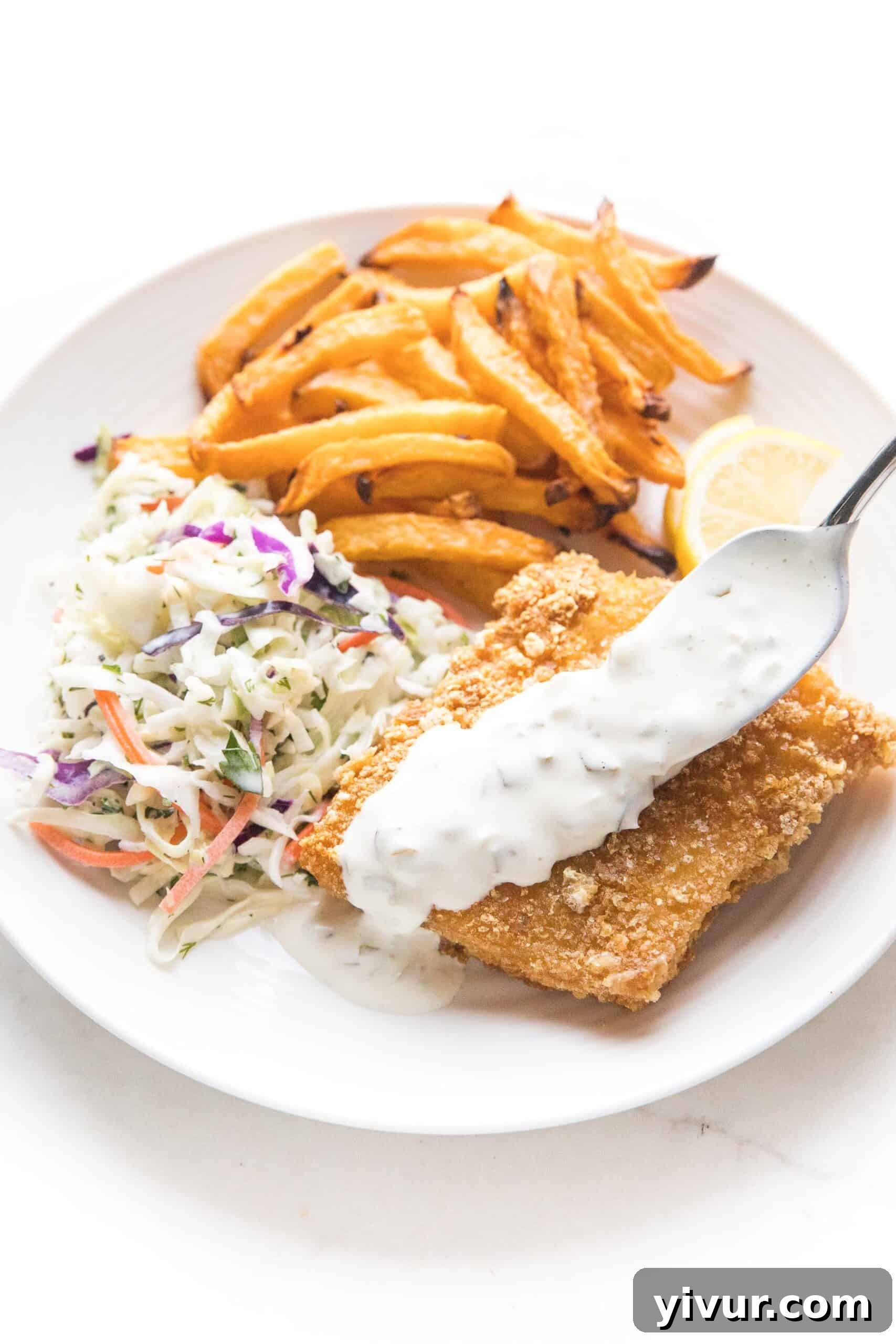 Crispy keto fish and chips served with coleslaw and tartar sauce on a white plate, showcasing its golden perfection.