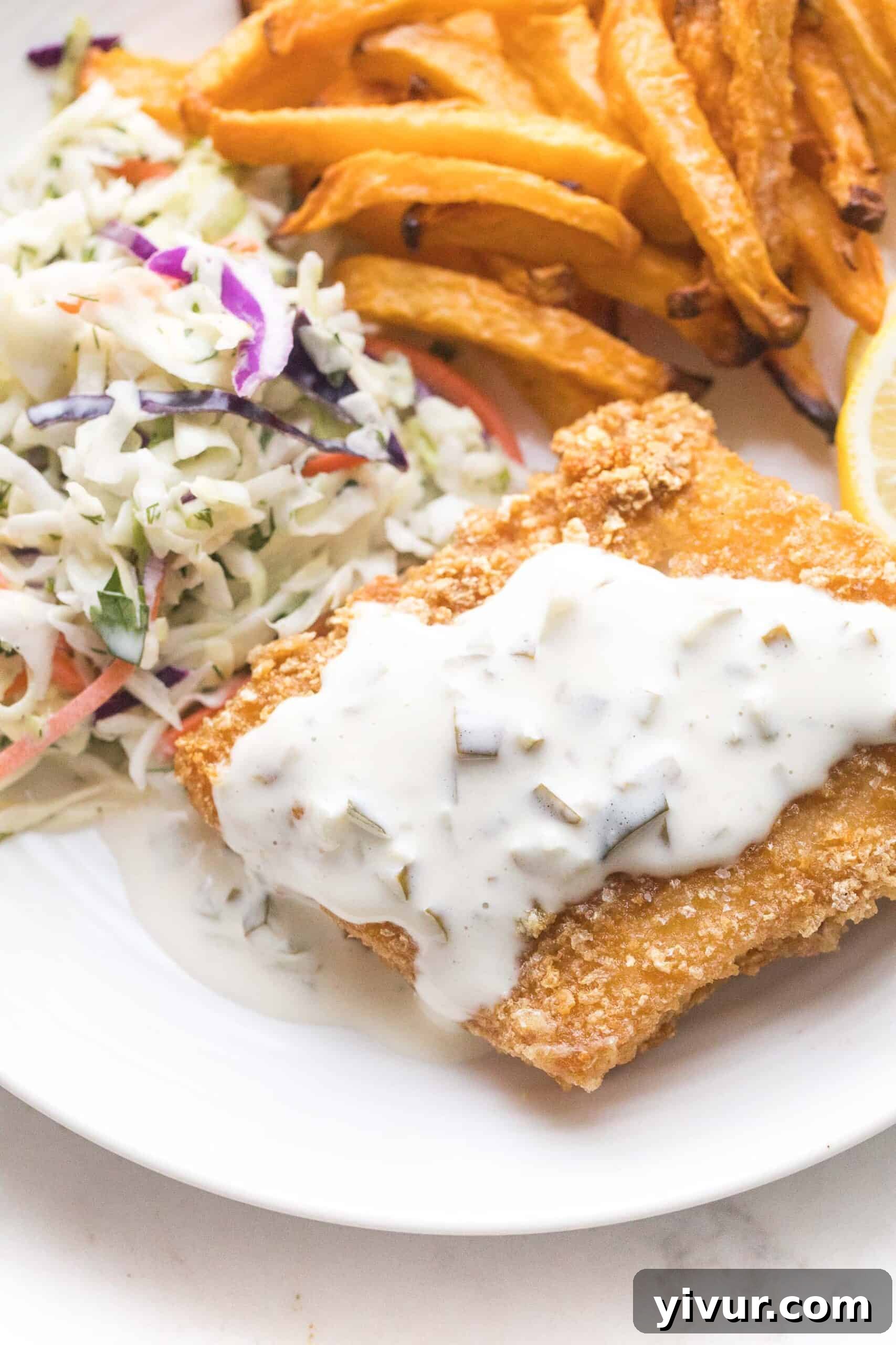 Pan-fried pork panko crusted fish with tartar sauce and coleslaw, plated for serving. The golden brown fish is crisp and inviting.