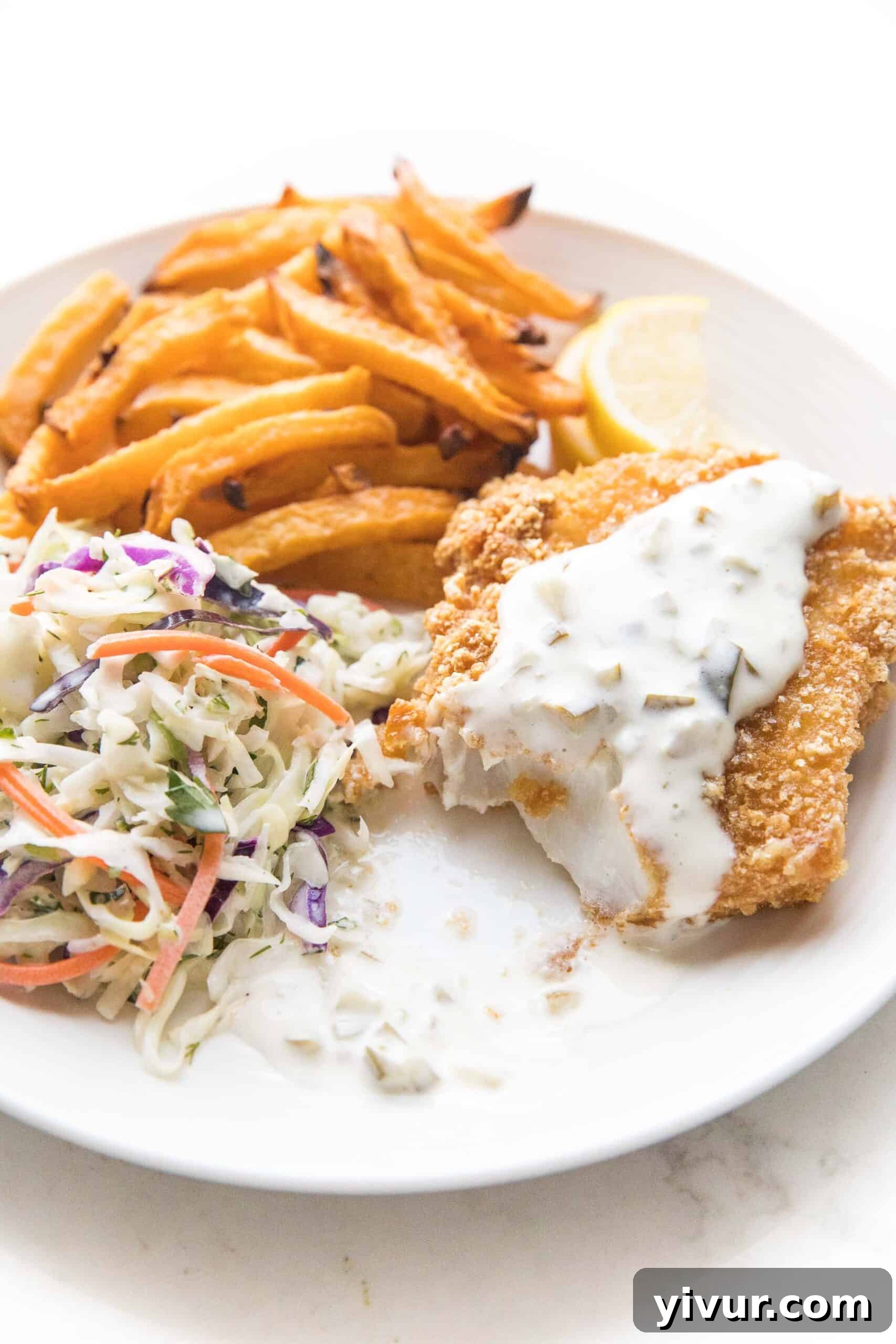 Close-up of crispy Whole30 fish and chips showing crunchy pork rind coating on a white plate with lemon wedges and fresh herbs.