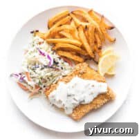 Crispy keto fish and chips with coleslaw and tartar sauce on a white plate, showcasing the complete meal.