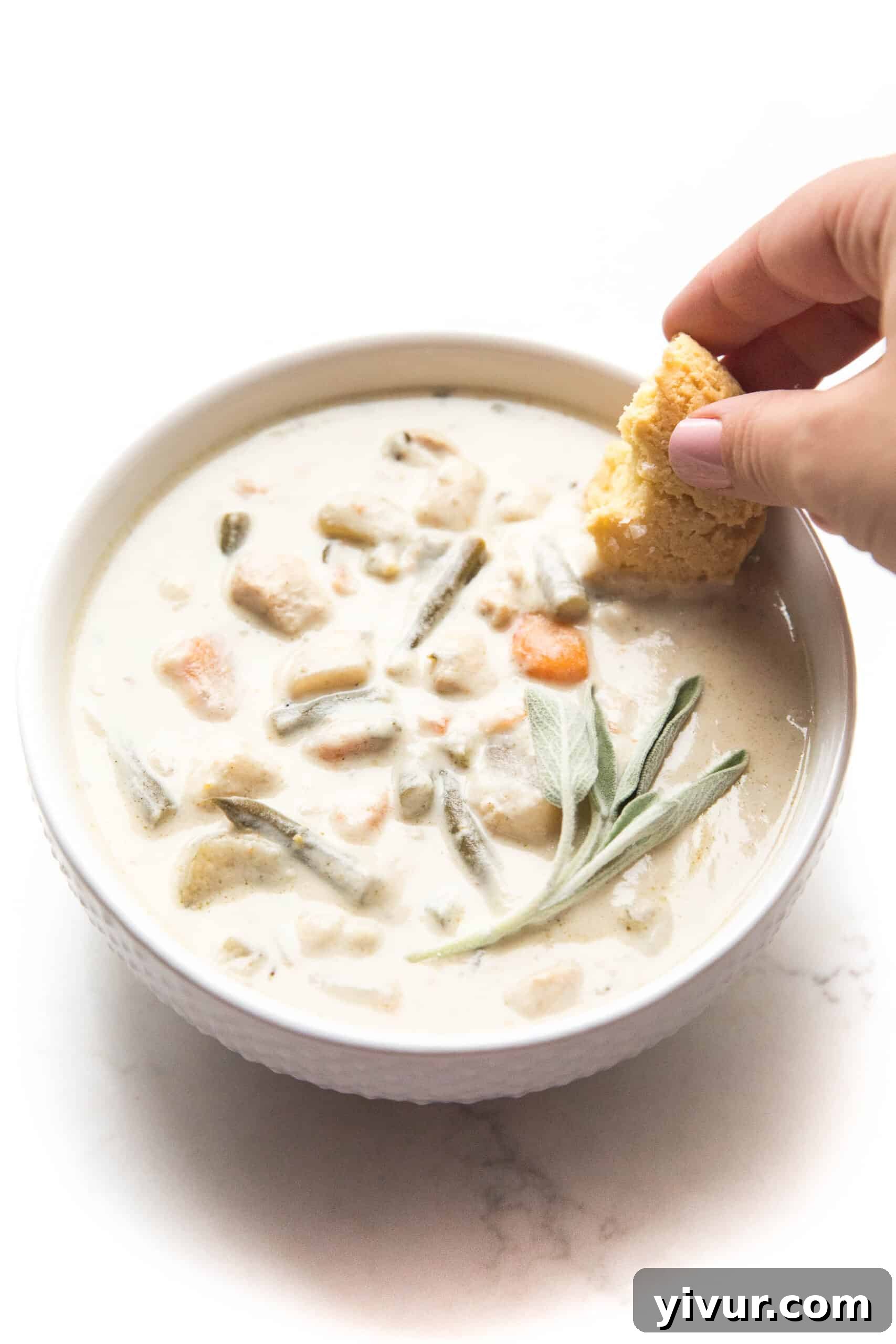 dipping a keto biscuit in creamy chicken chowder in a white bowl with a rustic background