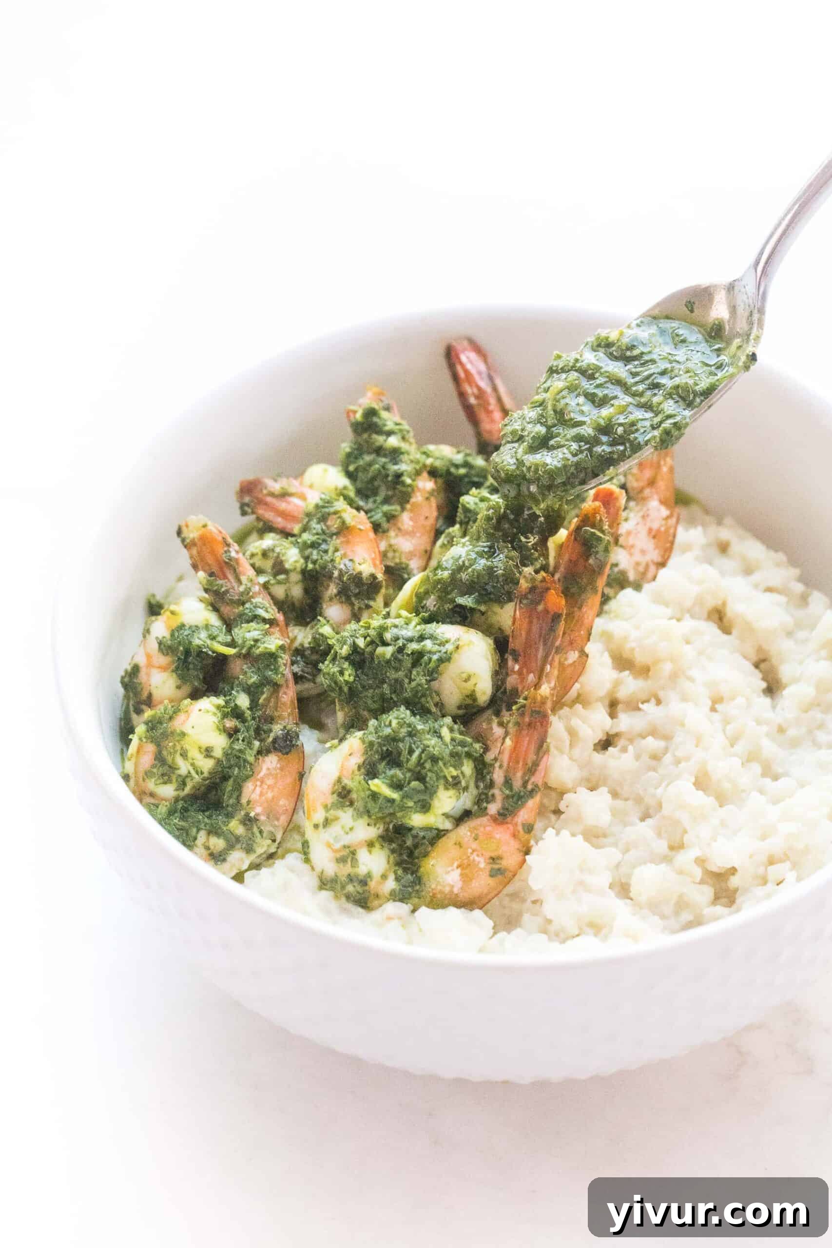 A hand pouring a generous amount of fresh chimichurri sauce over cooked shrimp served with cauliflower rice risotto, enhancing its flavor.