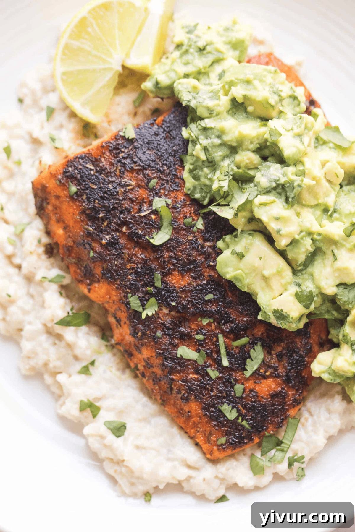 Photo of perfectly cooked keto blackened salmon with chunky guacamole on a bed of cauliflower rice, garnished with fresh lime.