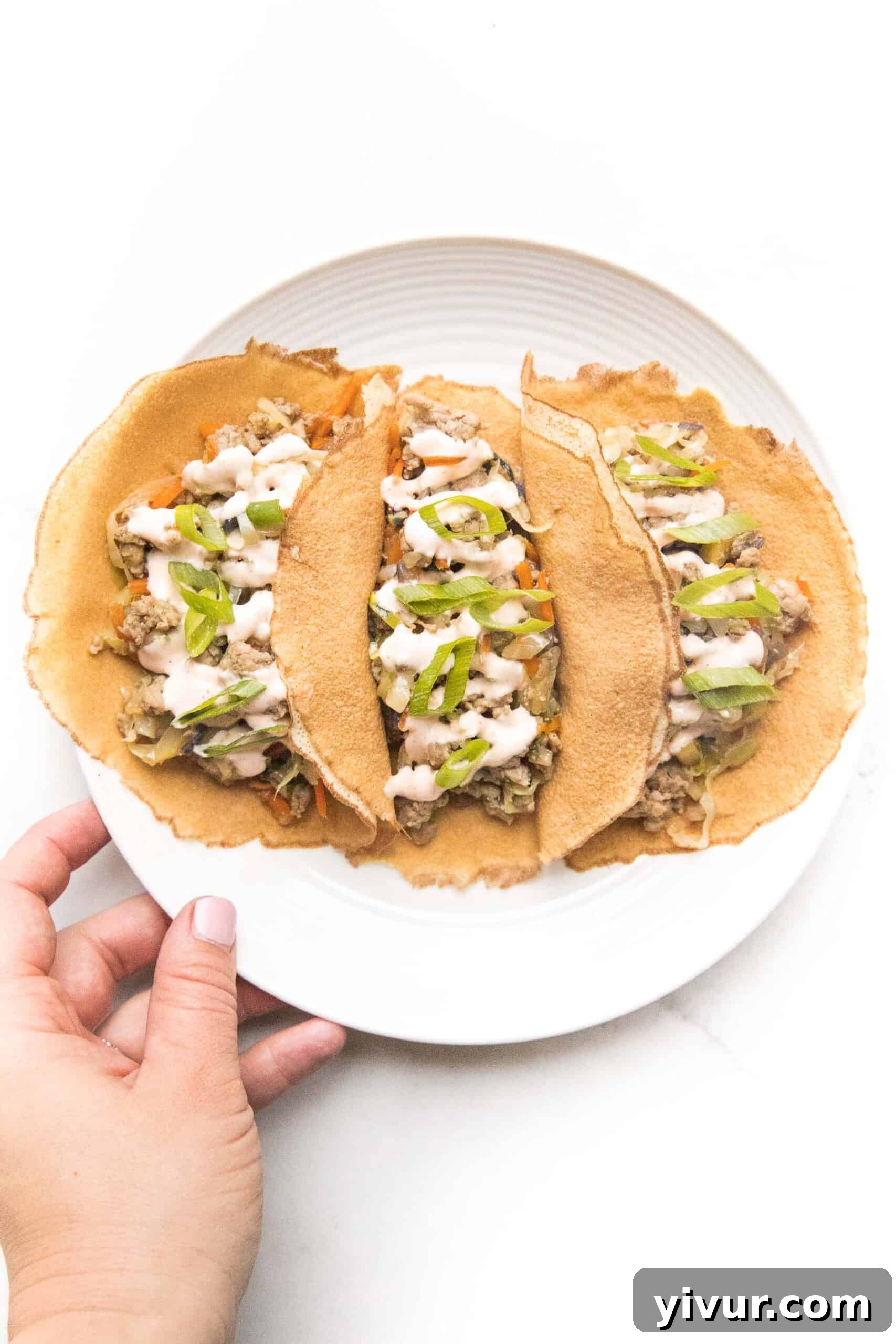 A hand holding a Mu Shu Pork wrap made with cauliflower, drizzled with sriracha mayo