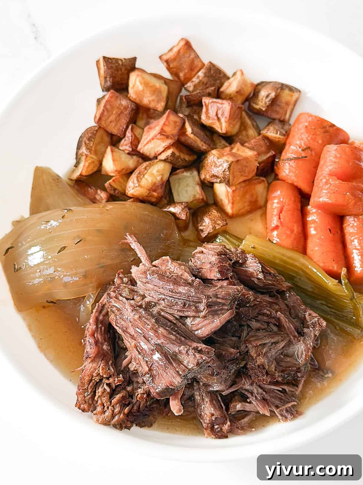 pot roast on a white plate with carrots, celery, onions and crispy roasted potatoes