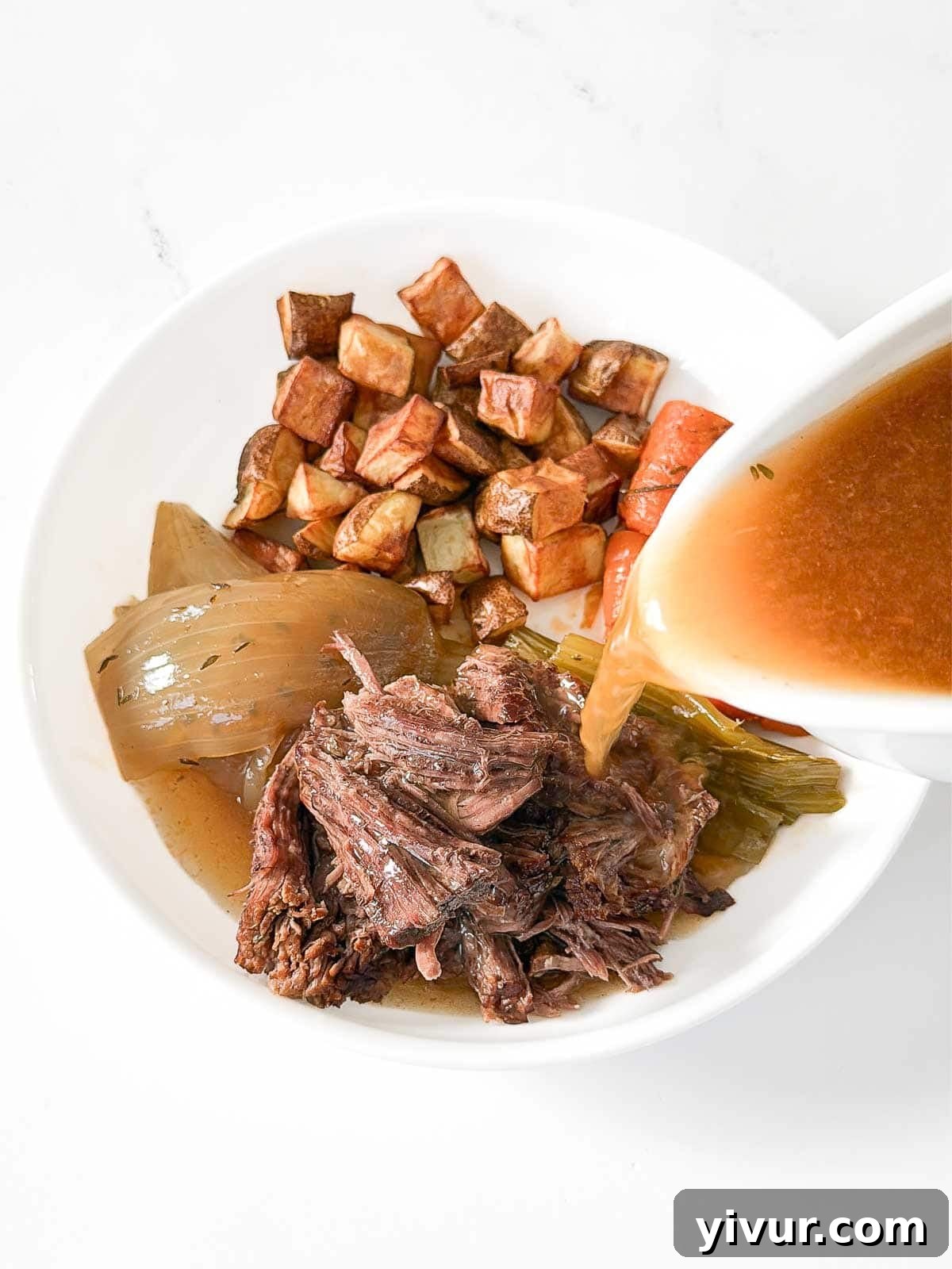 Pouring pot roast juices over a plate of pot roast and veggies