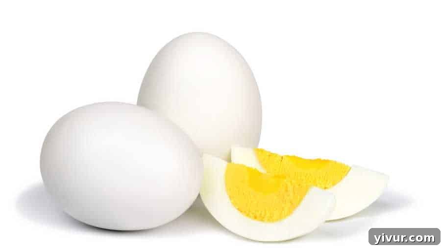 A perfectly peeled hard-boiled egg, cut in half to show its firm yolk, placed on a pristine white background, symbolizing a simple yet highly nutritious snack.