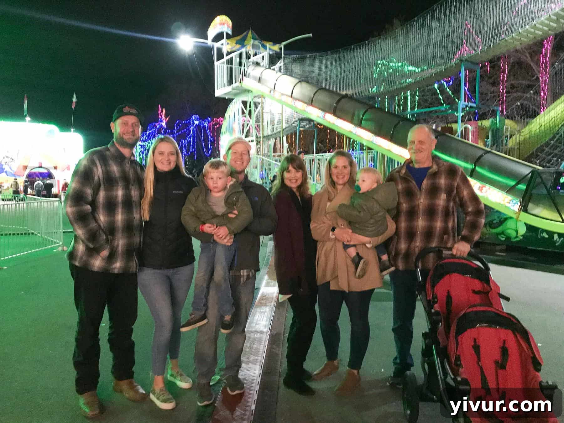 A family enjoying a Christmas light show at the fairgrounds, surrounded by festive decorations.