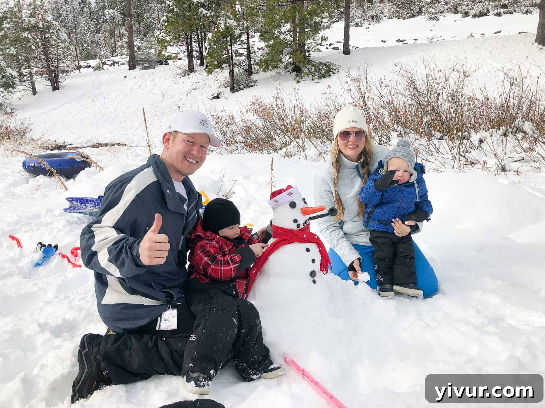 A family proudly posing next to their freshly built snowman in a snowy landscape.