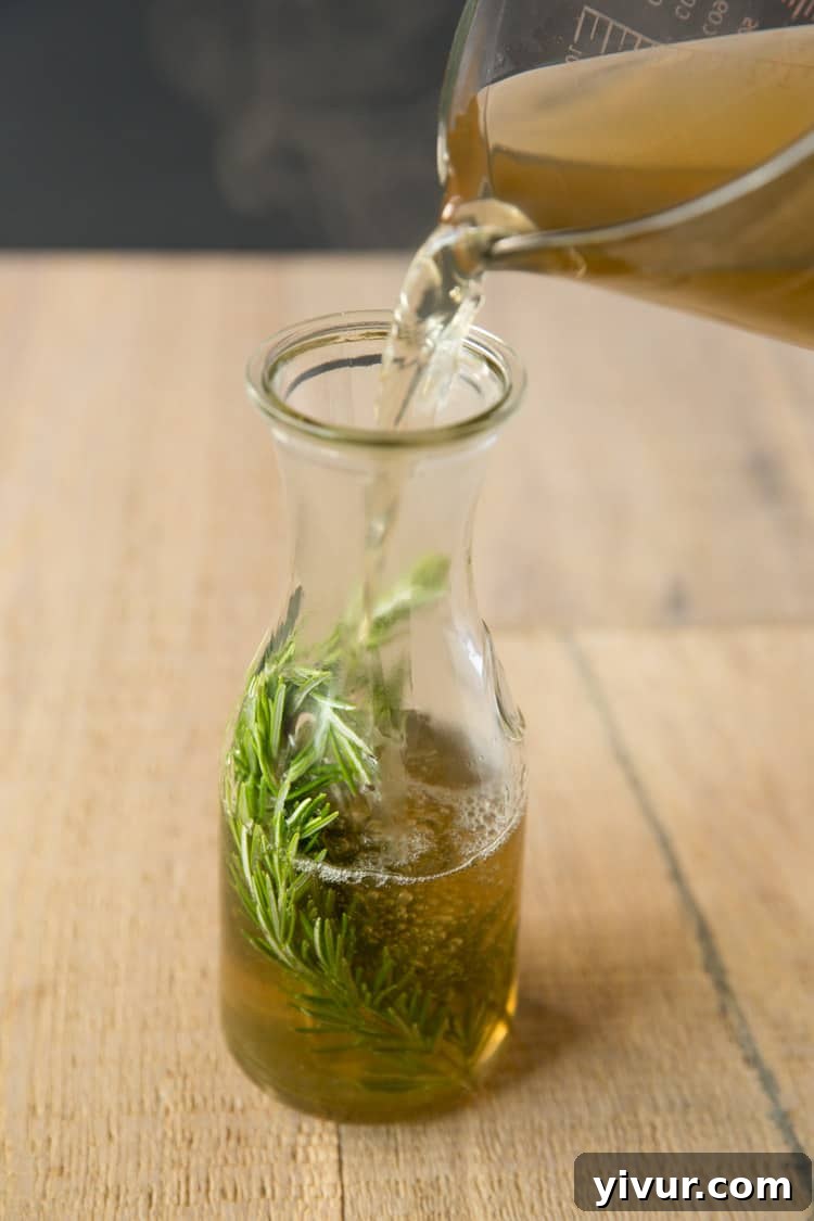 A measuring glass pouring freshly made rosemary simple syrup into a glass jar for storage.