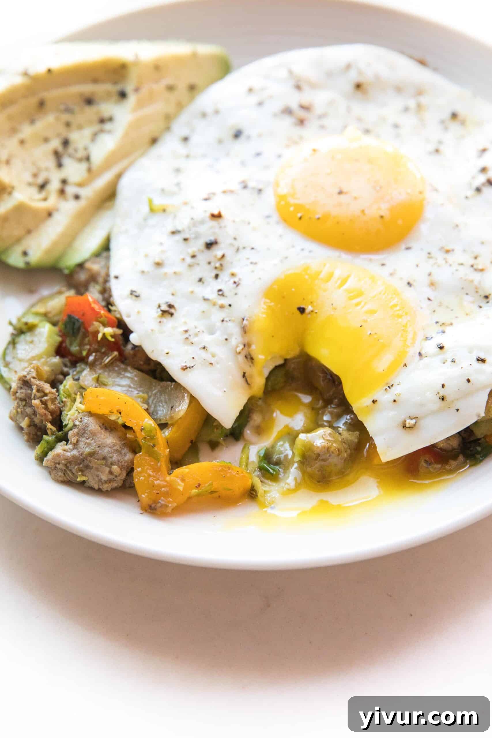 Sunny side up egg yolk dripping over a rich and flavorful Whole30 + Keto sausage and Brussels hash