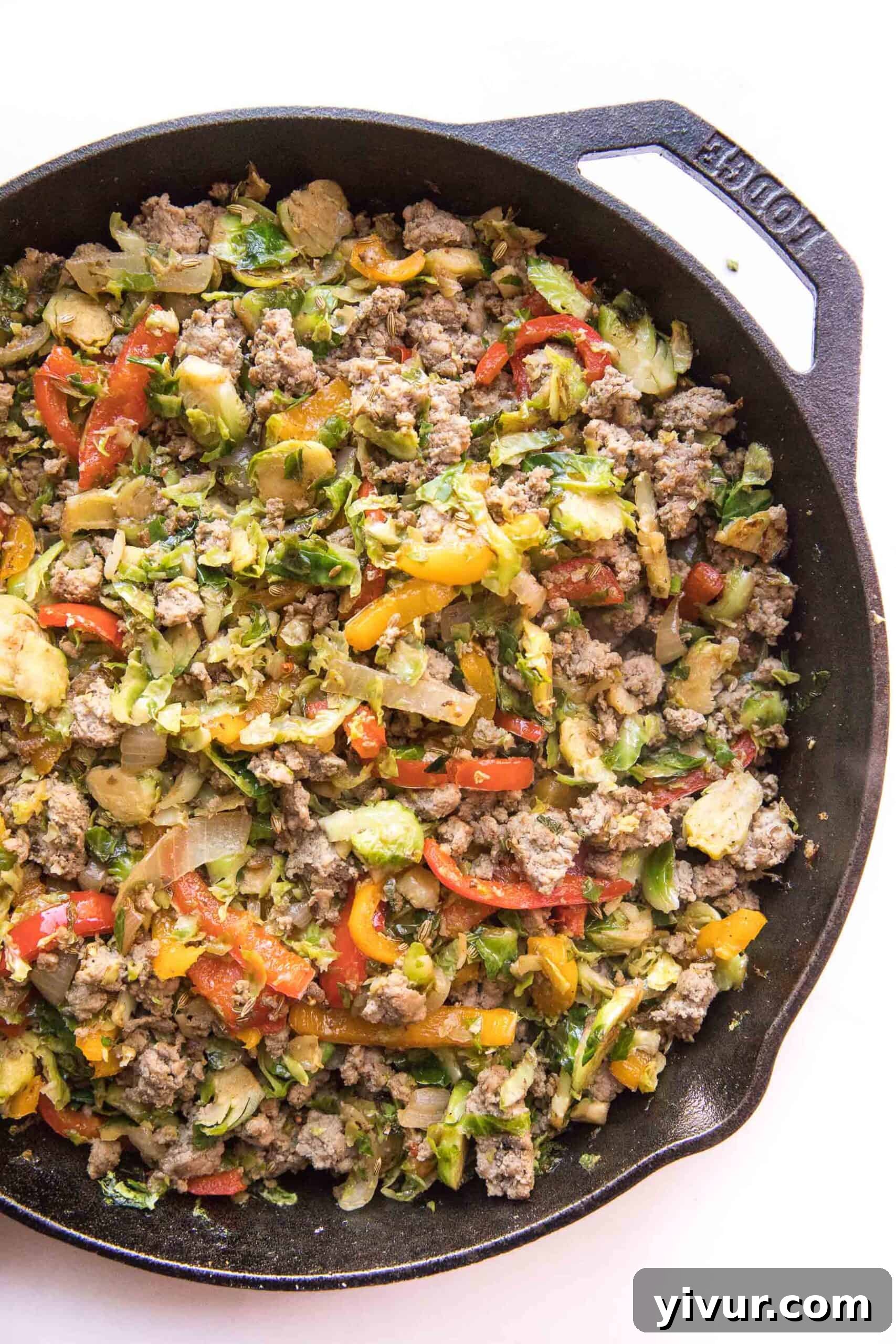 Hearty sausage and Brussels hash sizzling in a rustic cast iron skillet, showcasing fresh ingredients