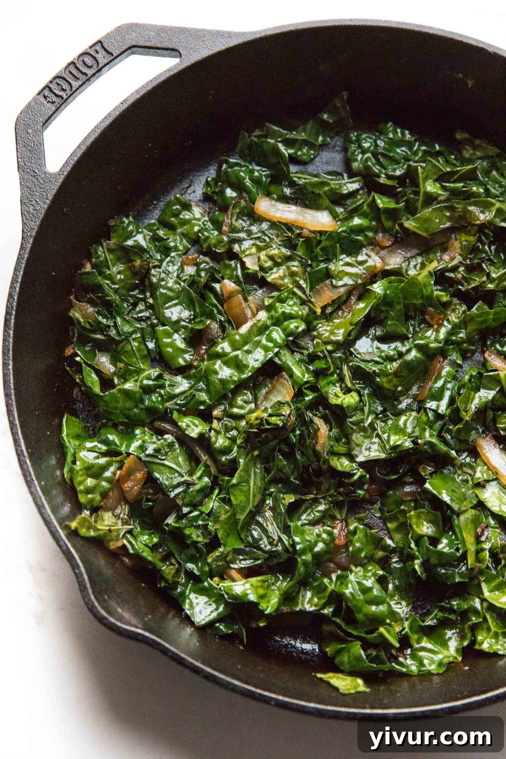Vibrant green sautéed kale in a cast iron skillet with golden onions and garlic