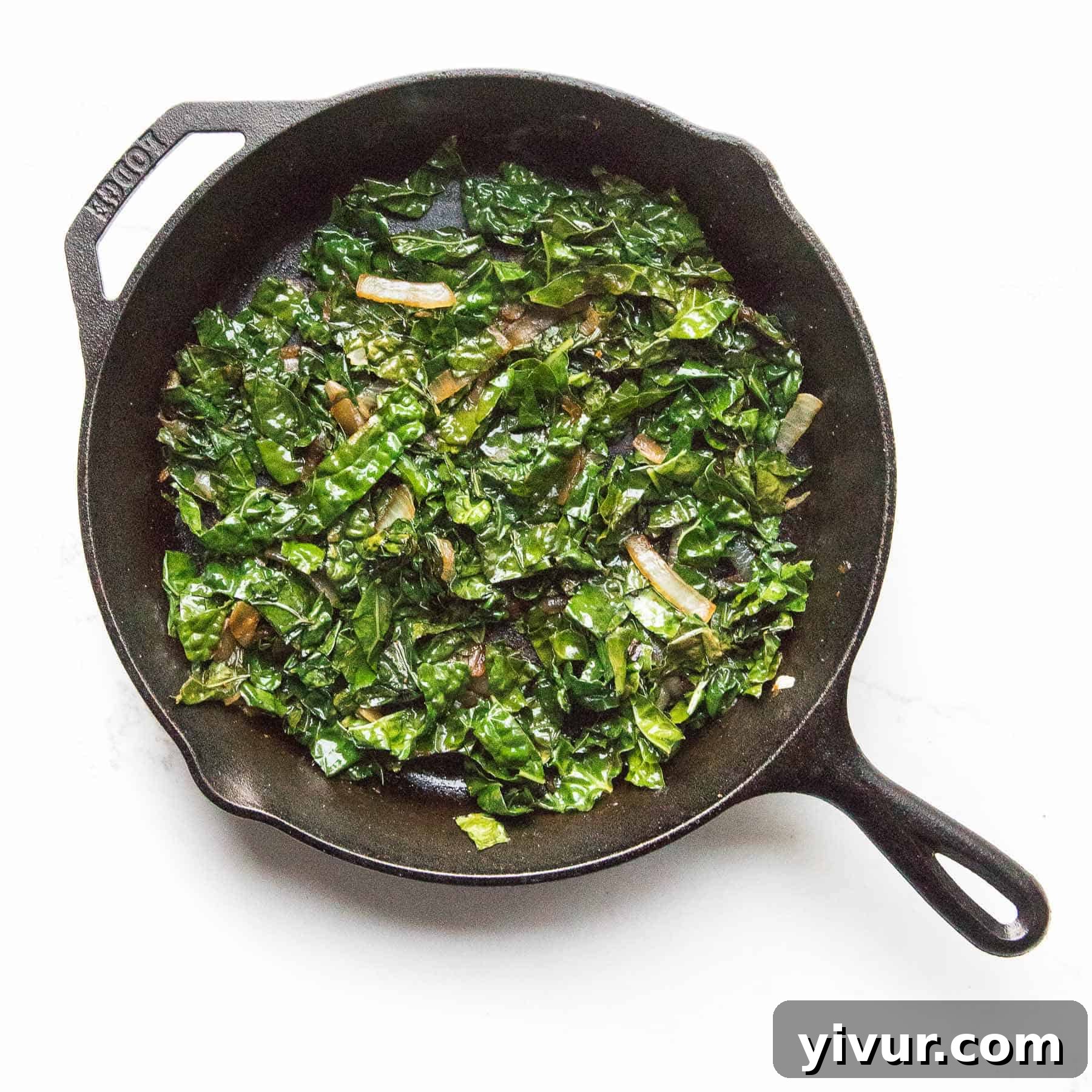 Close-up of freshly sautéed kale with visible onions and garlic cloves, ready to serve