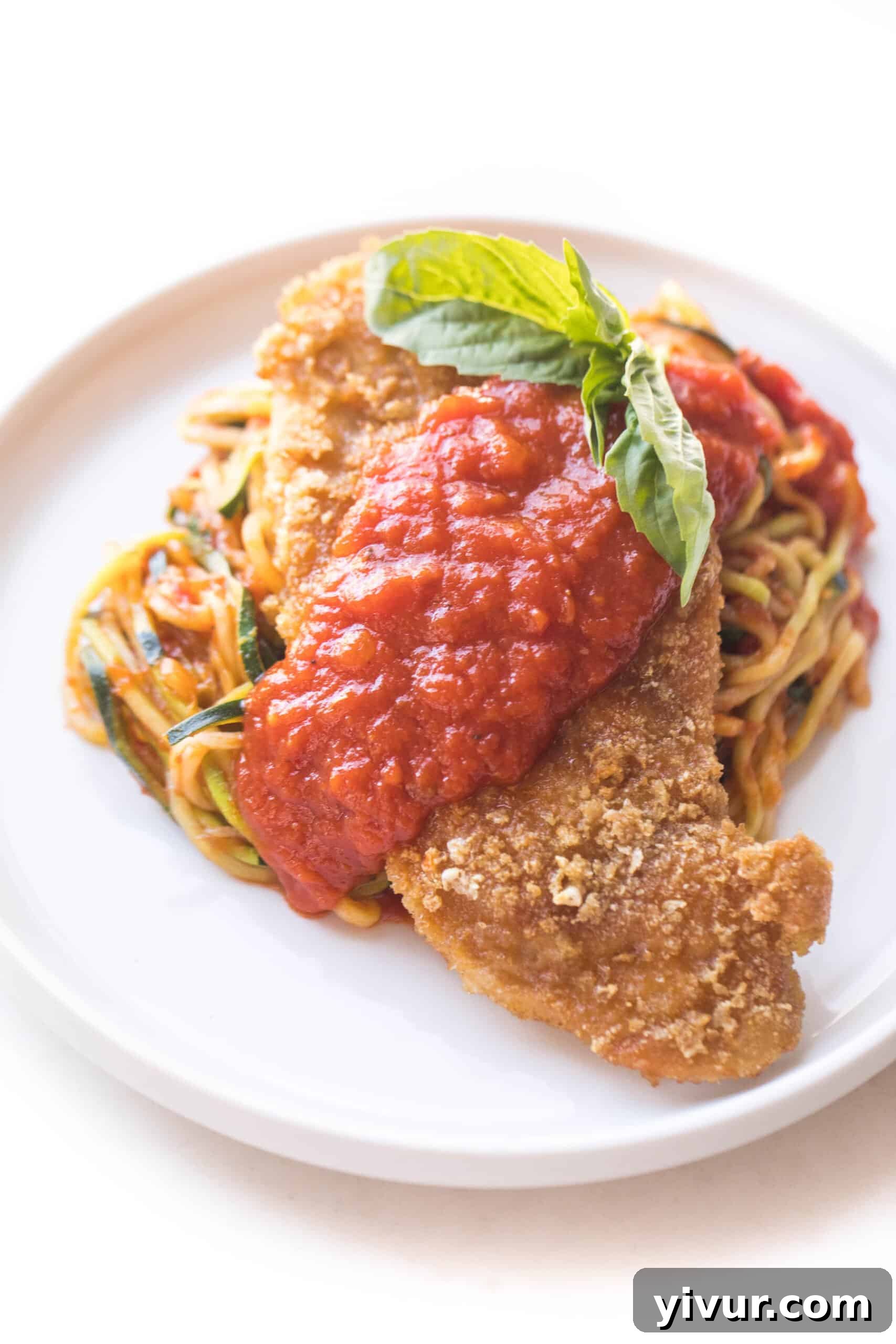 Crispy Whole30 Keto Chicken No-Parmesan topped with rich marinara sauce over a bed of fresh zucchini noodles on a white plate