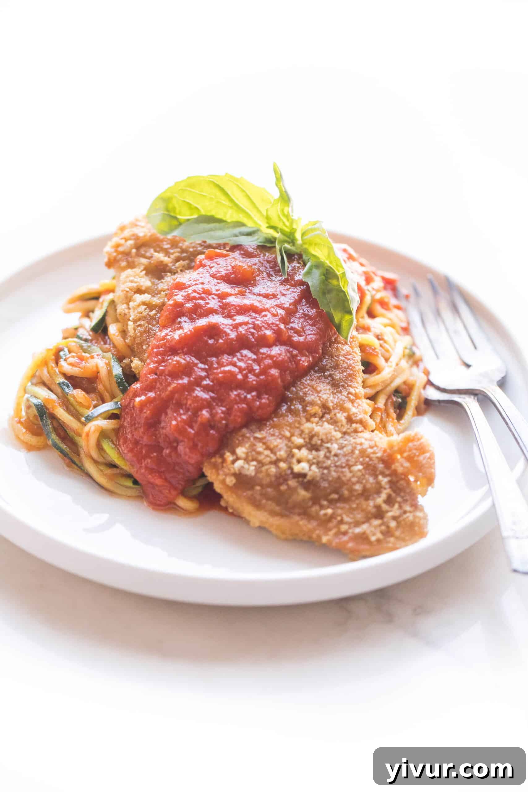Dairy-free Whole30 Keto Chicken No-Parmesan served with fresh zucchini noodles and vibrant marinara sauce, garnished with basil