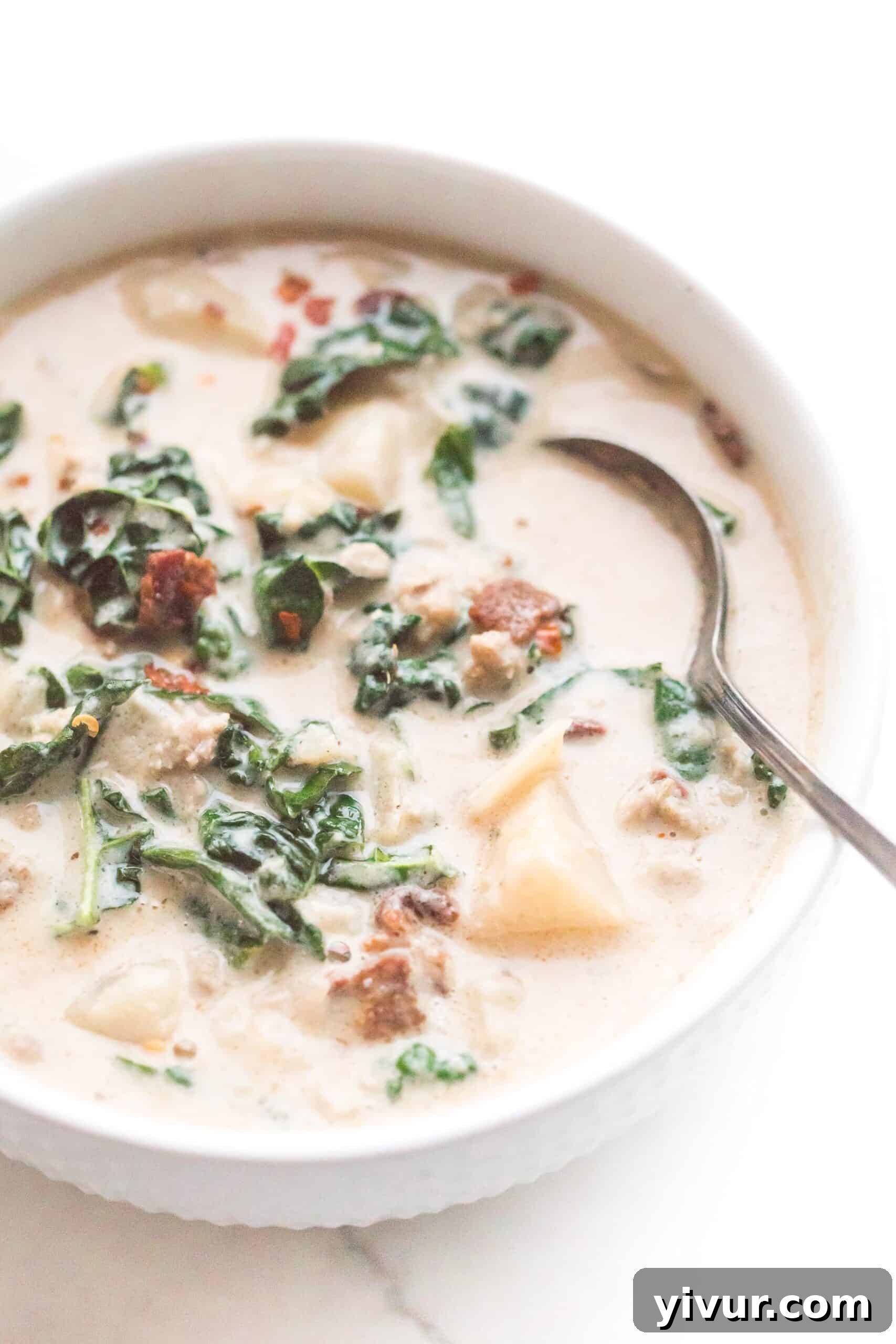 A spoon in a bowl of keto zuppa toscana with sausage, bacon, and kale in a creamy broth.