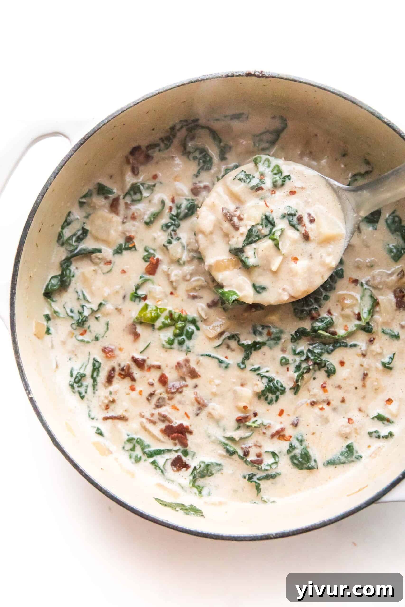 A ladle scooping creamy keto zuppa toscana from a soup pot, filled with sausage and kale.