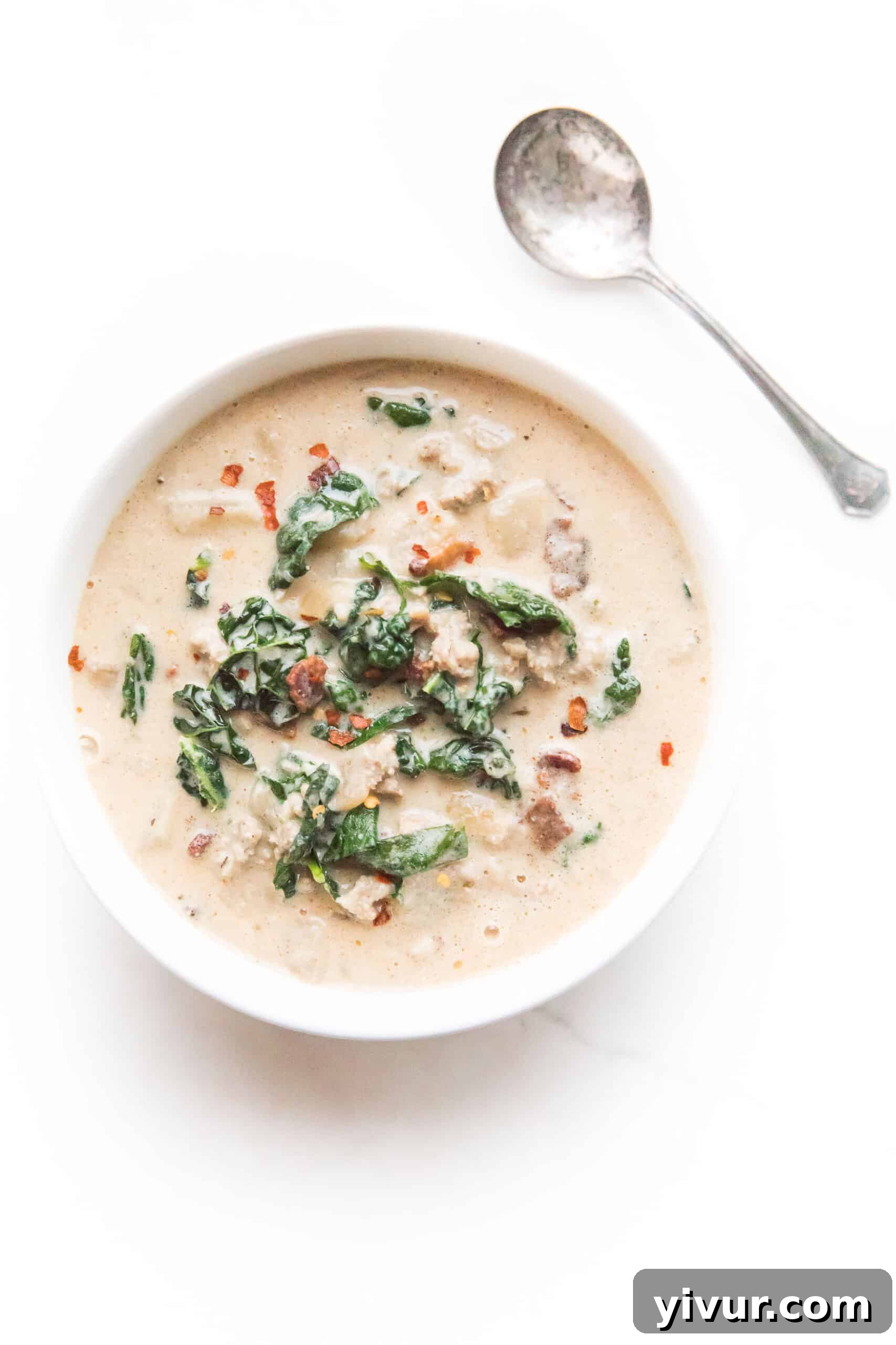 A bowl of Whole30 keto zuppa toscana with bacon and kale, with a spoon resting beside it.