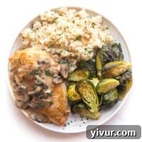 chicken with mushroom gravy on a white plate and background with roasted brussels sprouts and cauliflower rice