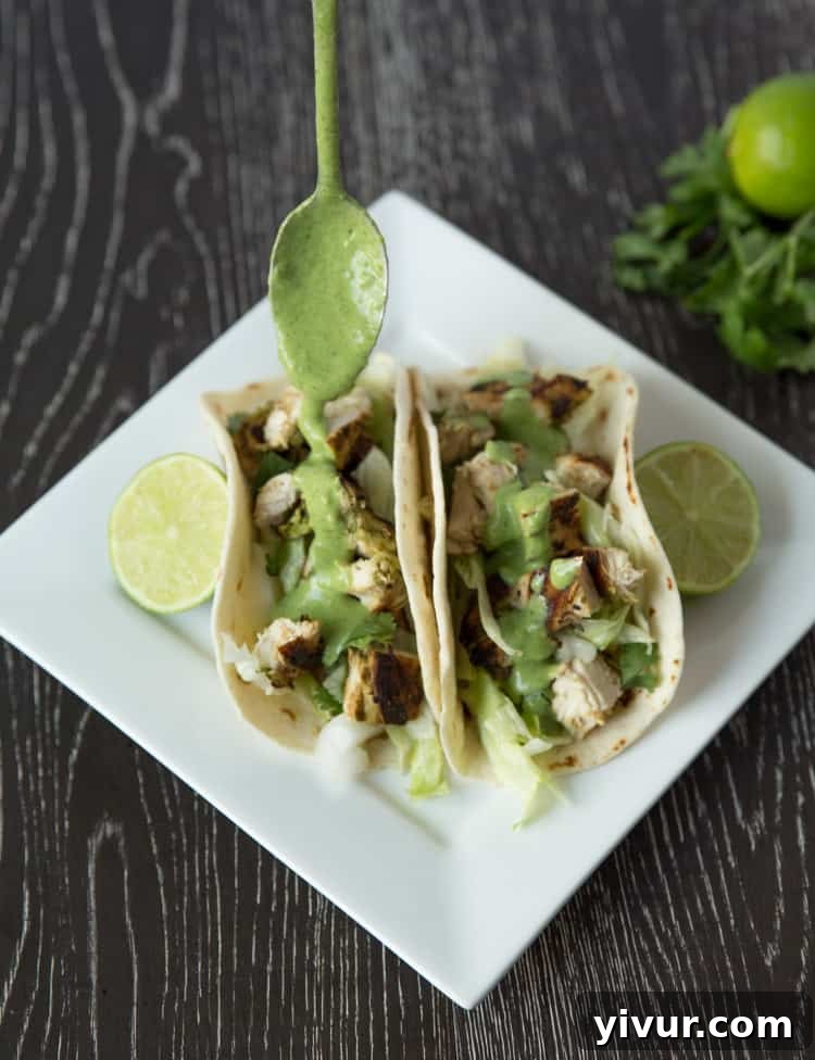 Three perfectly assembled chicken tacos on a plate, garnished with fresh cilantro and lime wedges