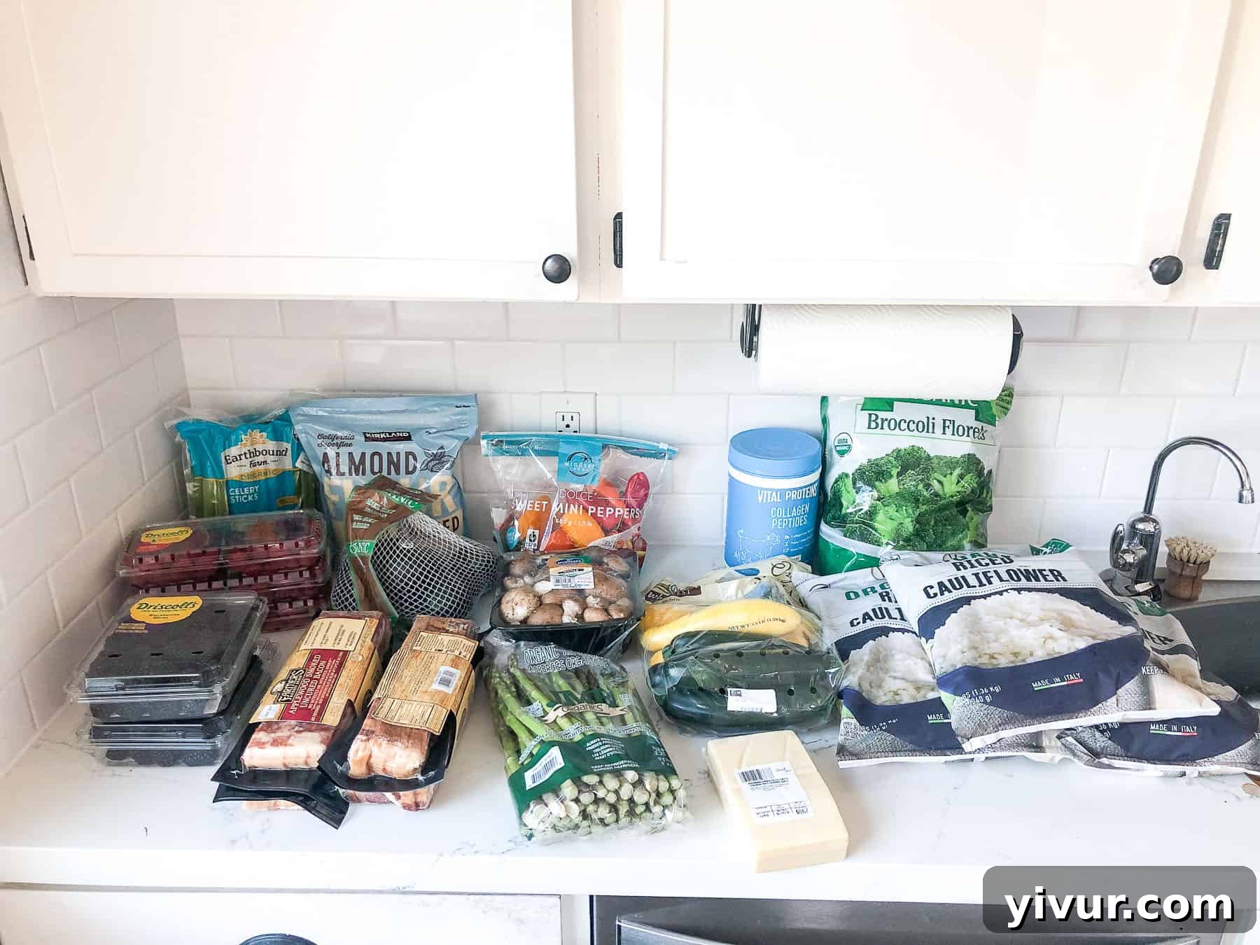 A wide variety of Whole30 and Keto friendly groceries from Costco, including fresh produce, bulk meats, and pantry staples, laid out after a shopping trip.