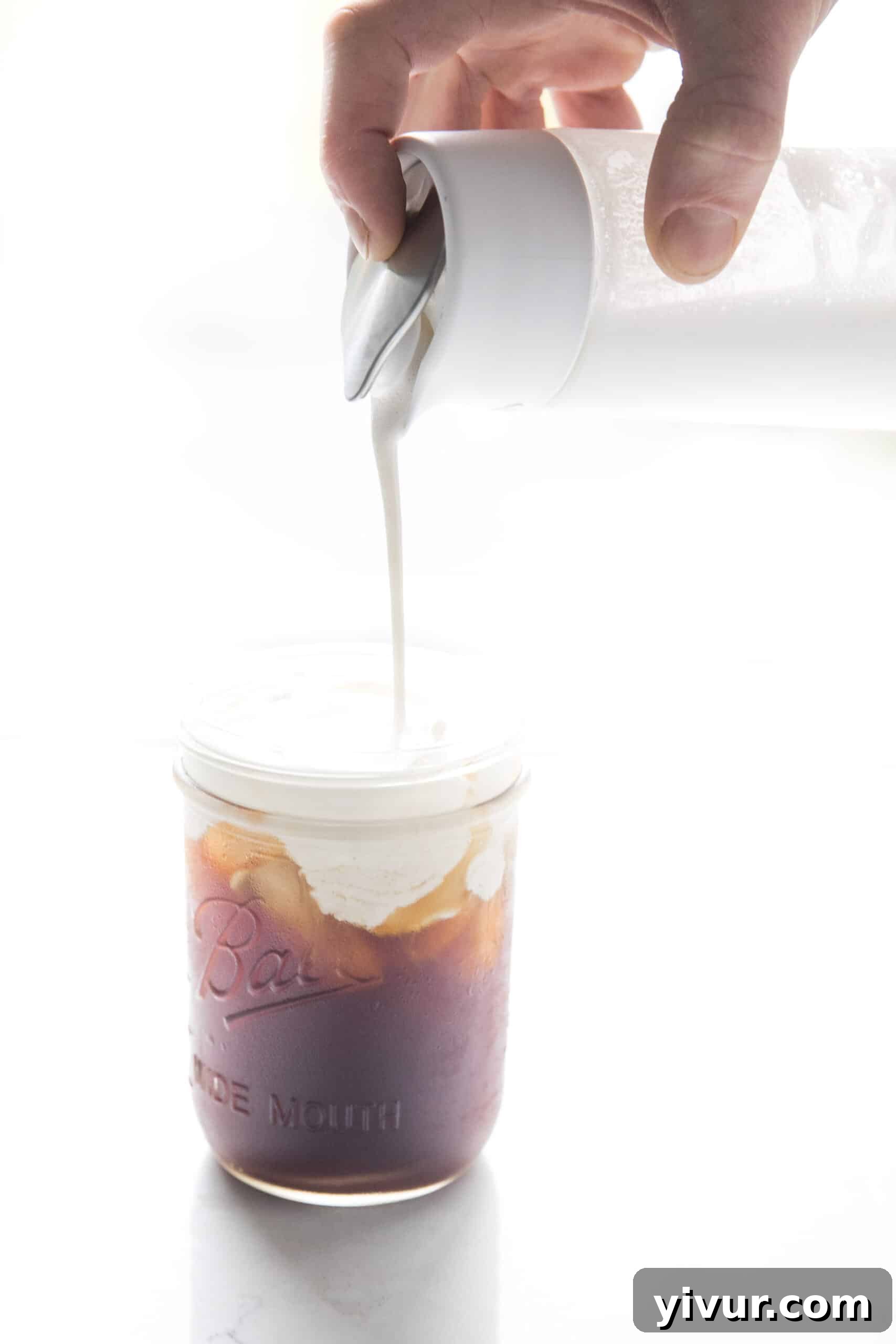 Homemade dairy-free heavy cream being poured over cold brew coffee, showcasing its rich, creamy texture.