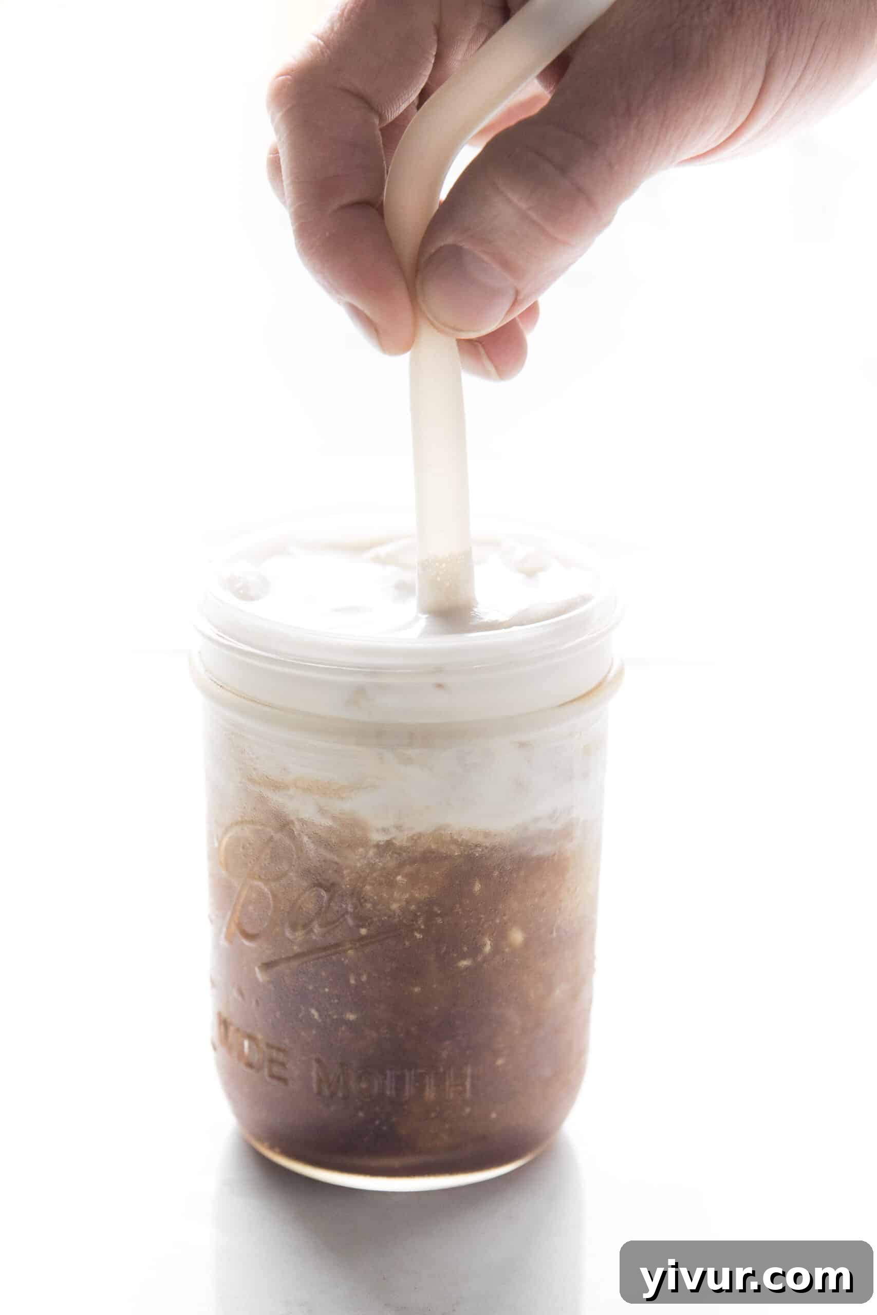 A mason jar of cold brew coffee being stirred with a spoon, highlighting the blending of vegan heavy cream.