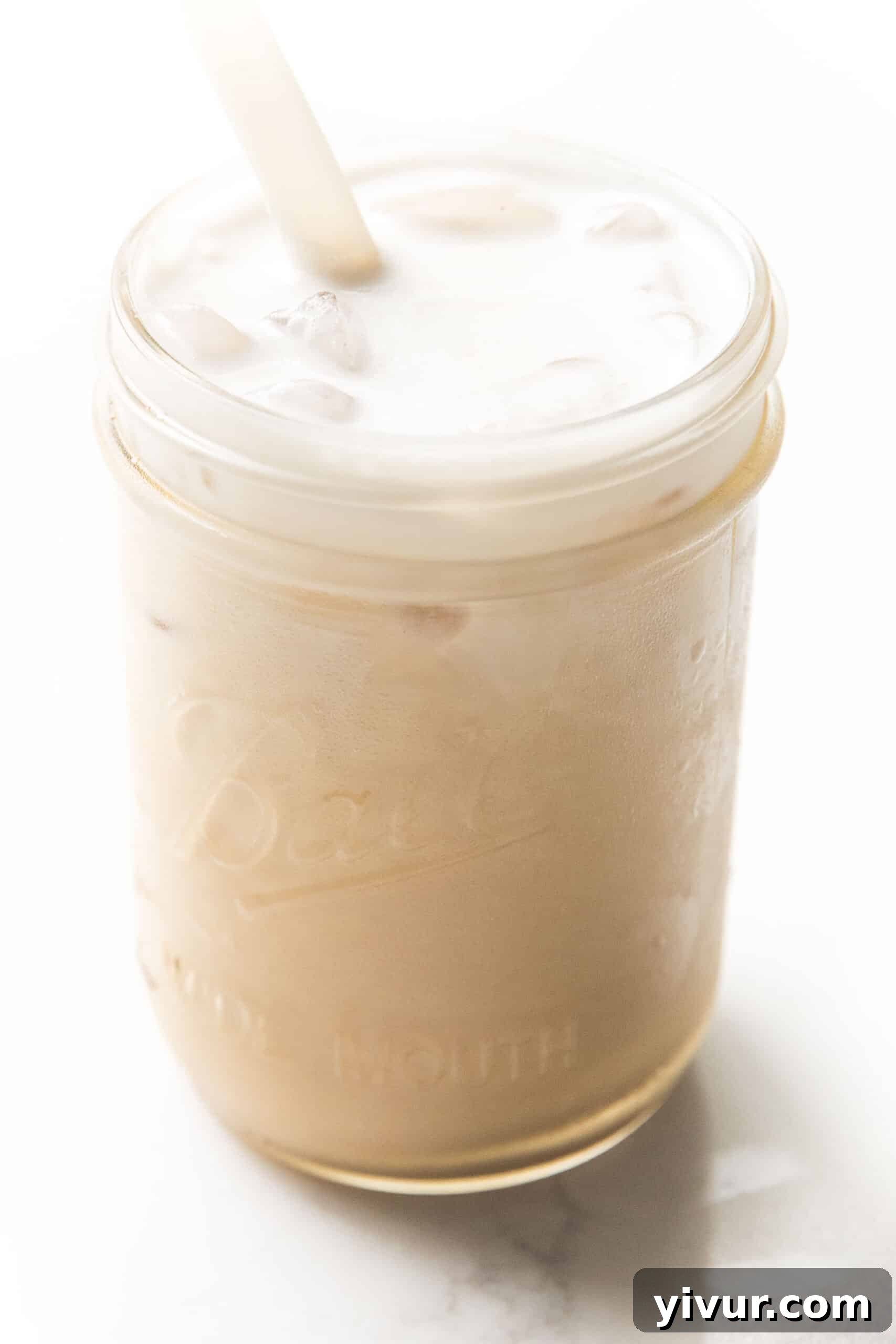 A mason jar filled with creamy dairy-free heavy cream, served alongside cold brew coffee with ice.