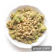 pesto cauliflower rice, broccoli, meatballs and pinenuts in a white bowl