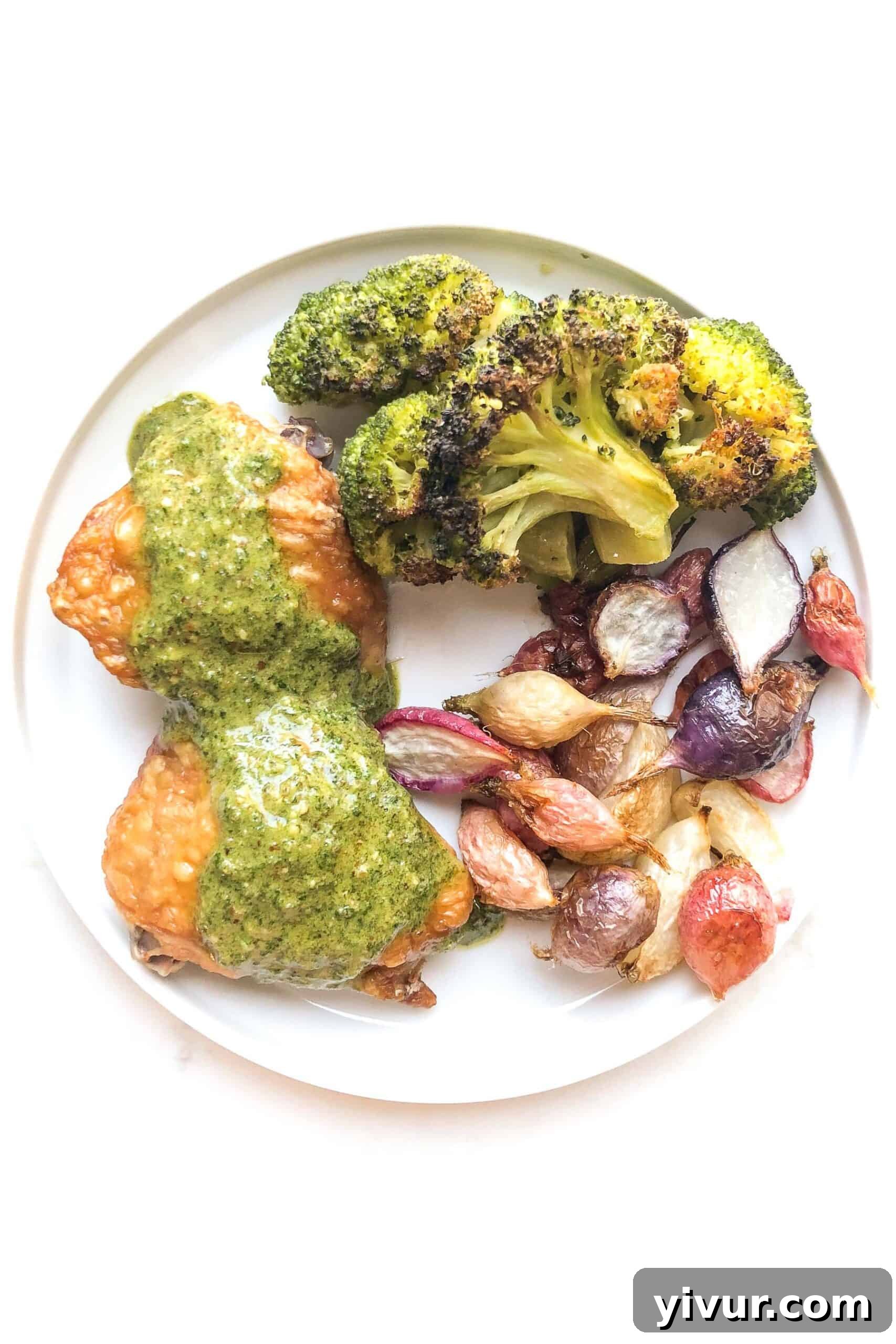 Crispy chicken thighs topped with a vibrant green orange parsley sauce, served alongside roasted radishes and roasted broccoli on a white plate