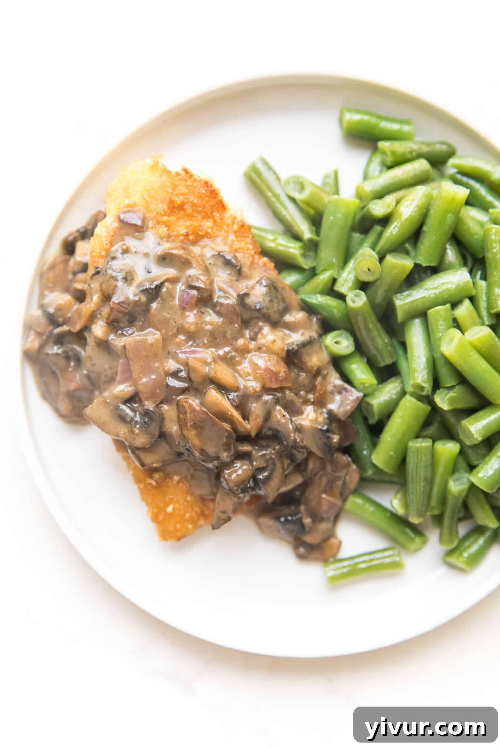 Crispy breaded chicken with creamy mushroom gravy served on a white plate with a side of green beans, perfect for Whole30 and Keto diets.