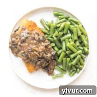 Crispy breaded chicken with mushroom gravy on a white plate with green beans