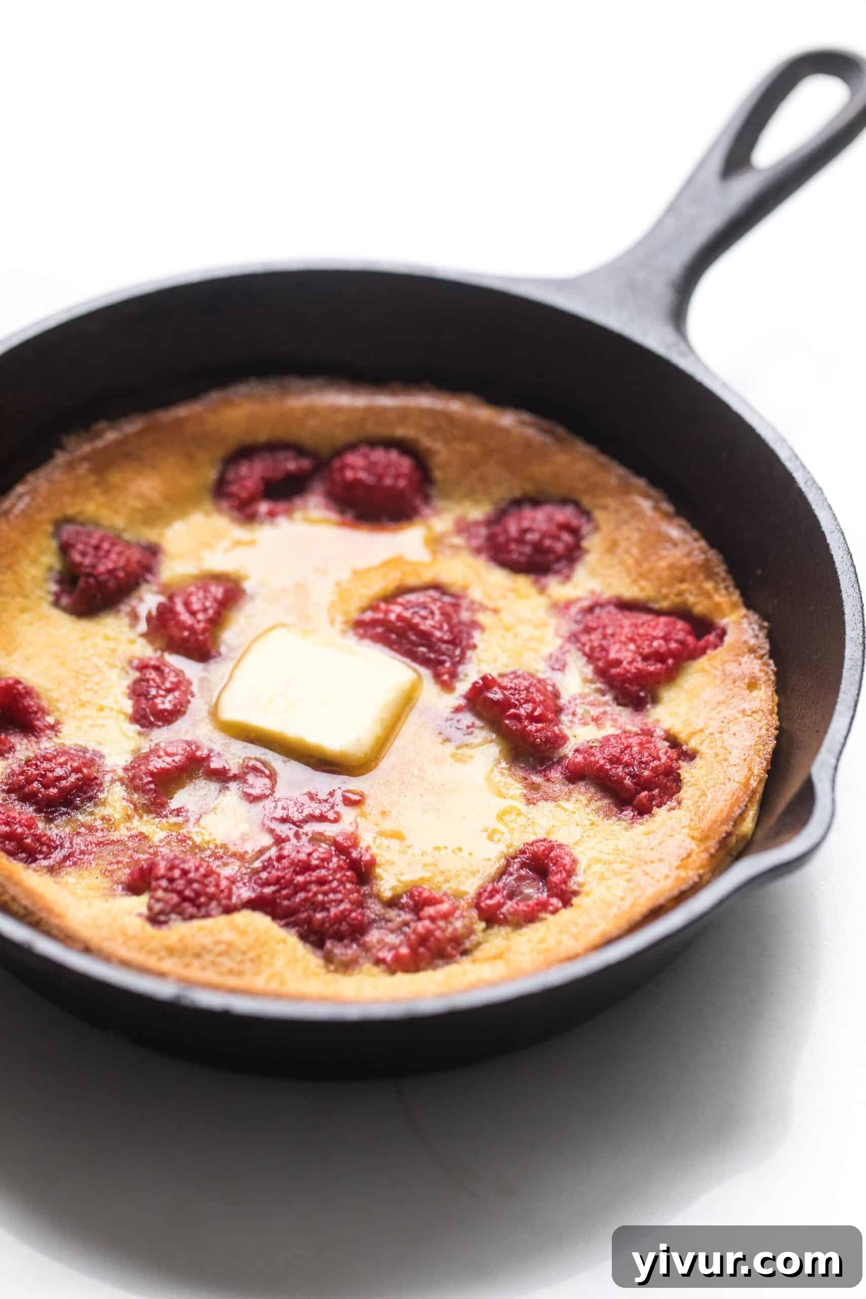 Keto Dutch Baby Pancake in a cast iron skillet with fresh raspberries and a dusting of powdered sweetener