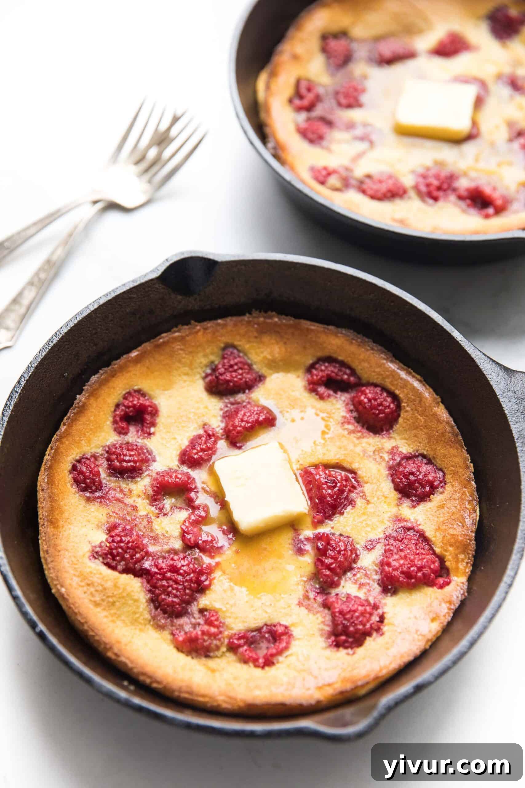 A whole Keto Dutch Baby Pancake with raspberries in a cast iron skillet