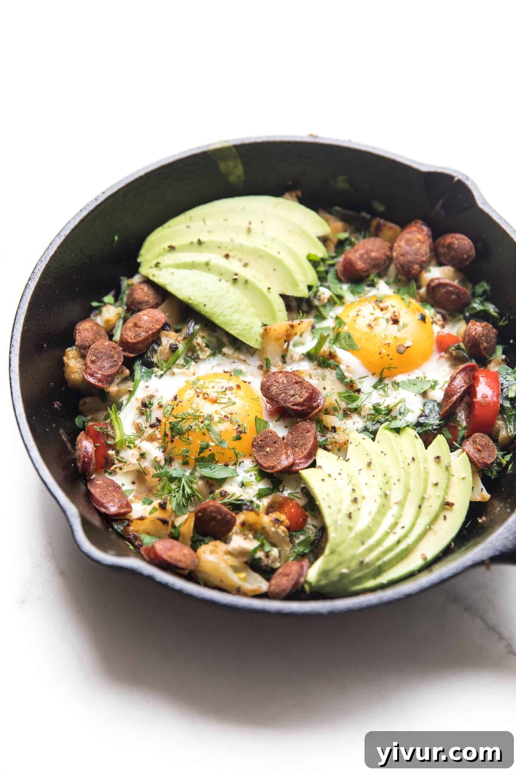 Delicious KETO low carb no potato breakfast hash with perfectly fried eggs and creamy avocado slices, served in a rustic cast iron skillet on a white background, highlighting healthy breakfast options.