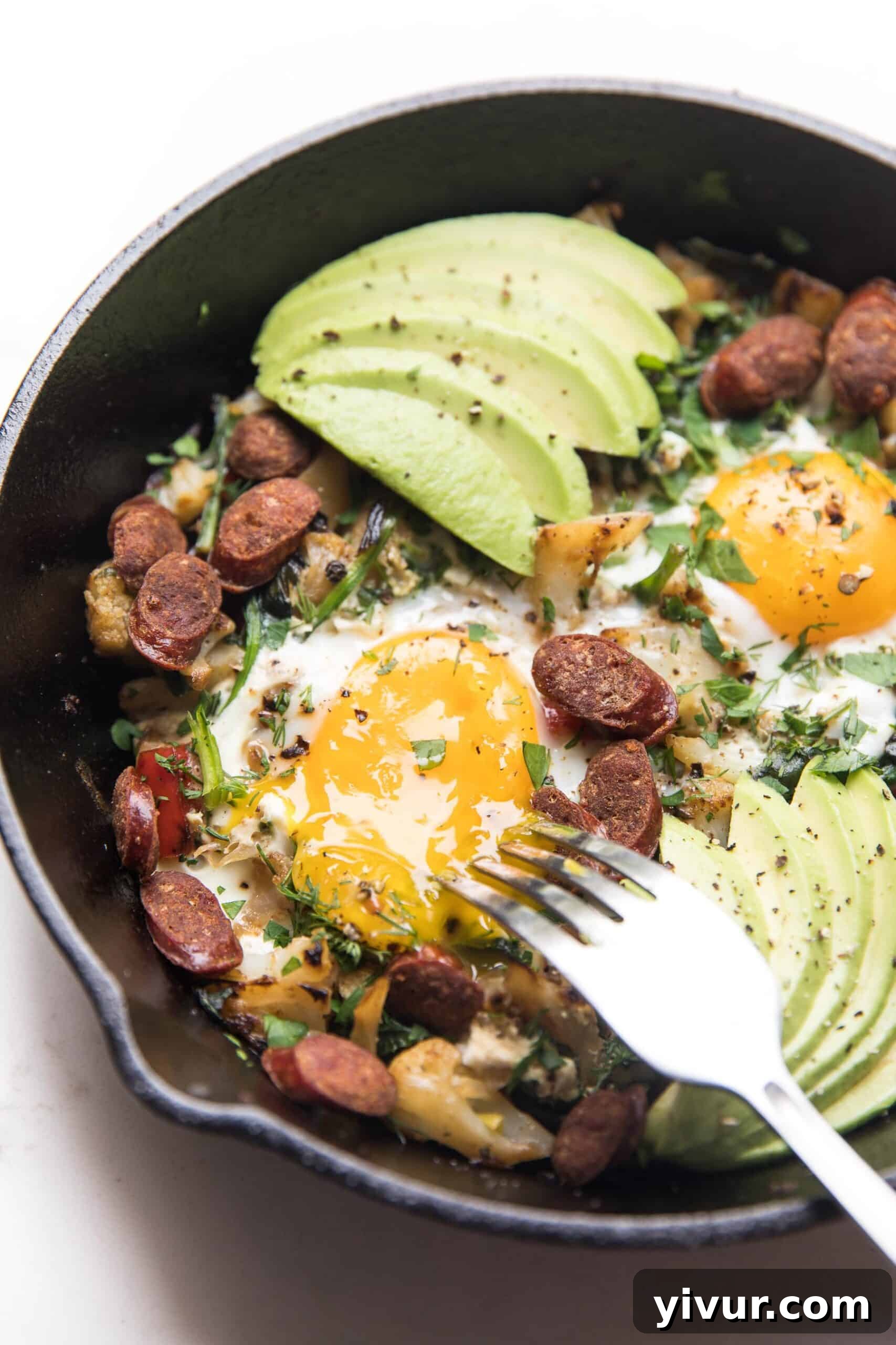 Close-up of a KETO low carb no potato breakfast hash in a cast iron skillet, featuring vibrant vegetables, sunny-side-up eggs, and avocado, perfect for healthy eating.