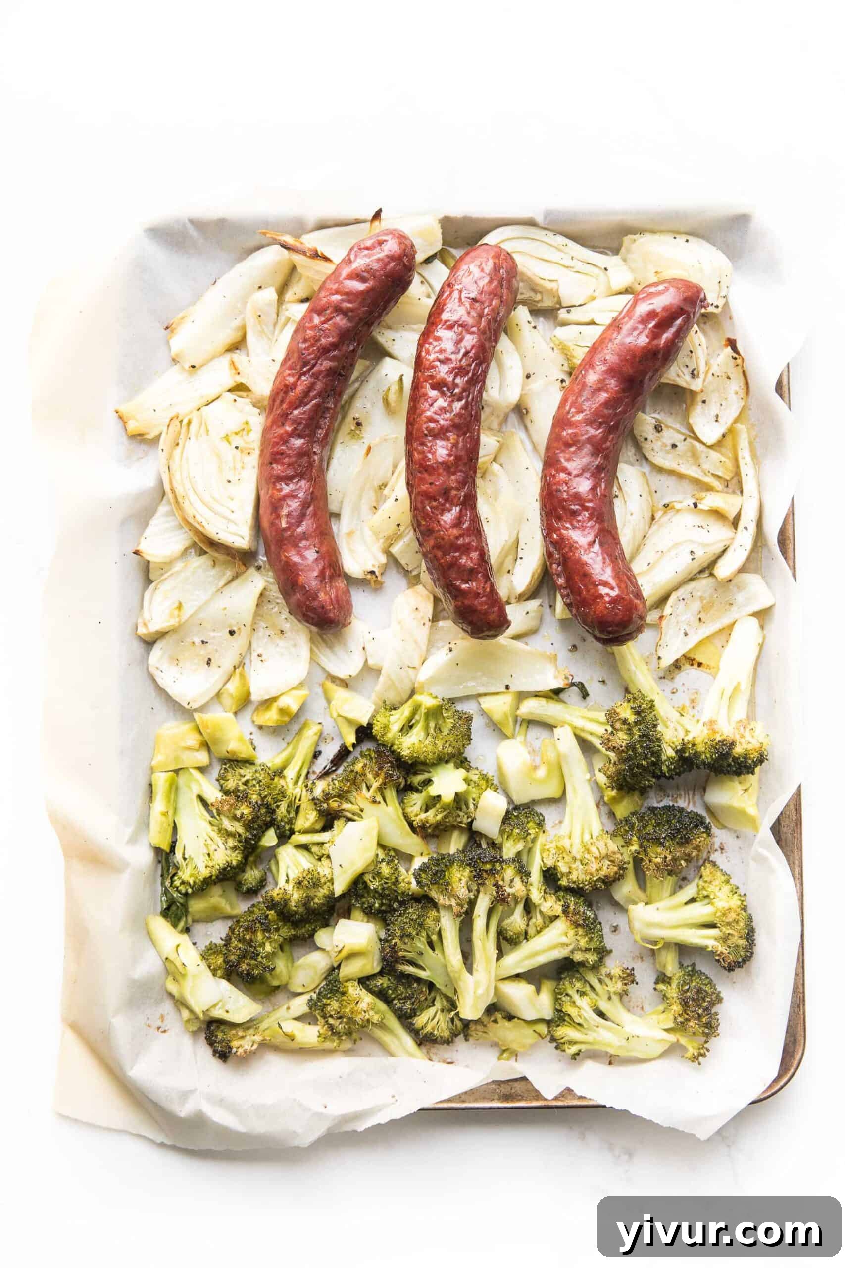 Raw sausage, chopped fennel, and broccoli arranged on a sheet pan ready for roasting