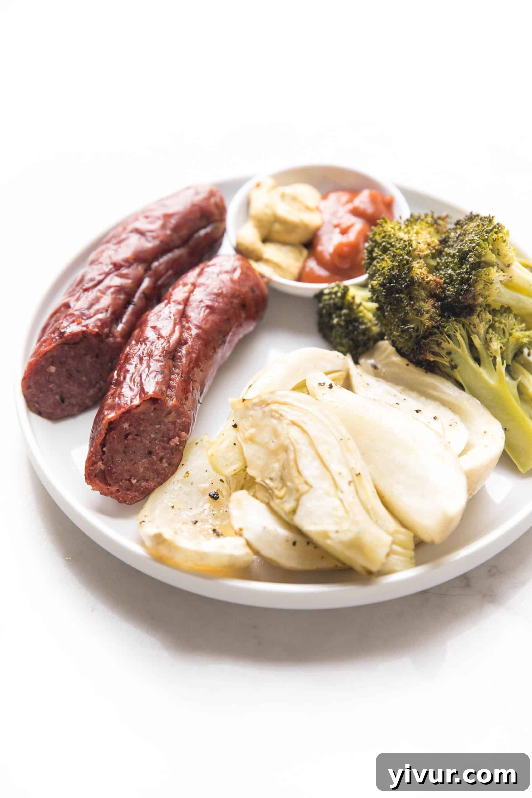 A close-up of roasted sausage, fennel, and broccoli on a white plate, ready to be served