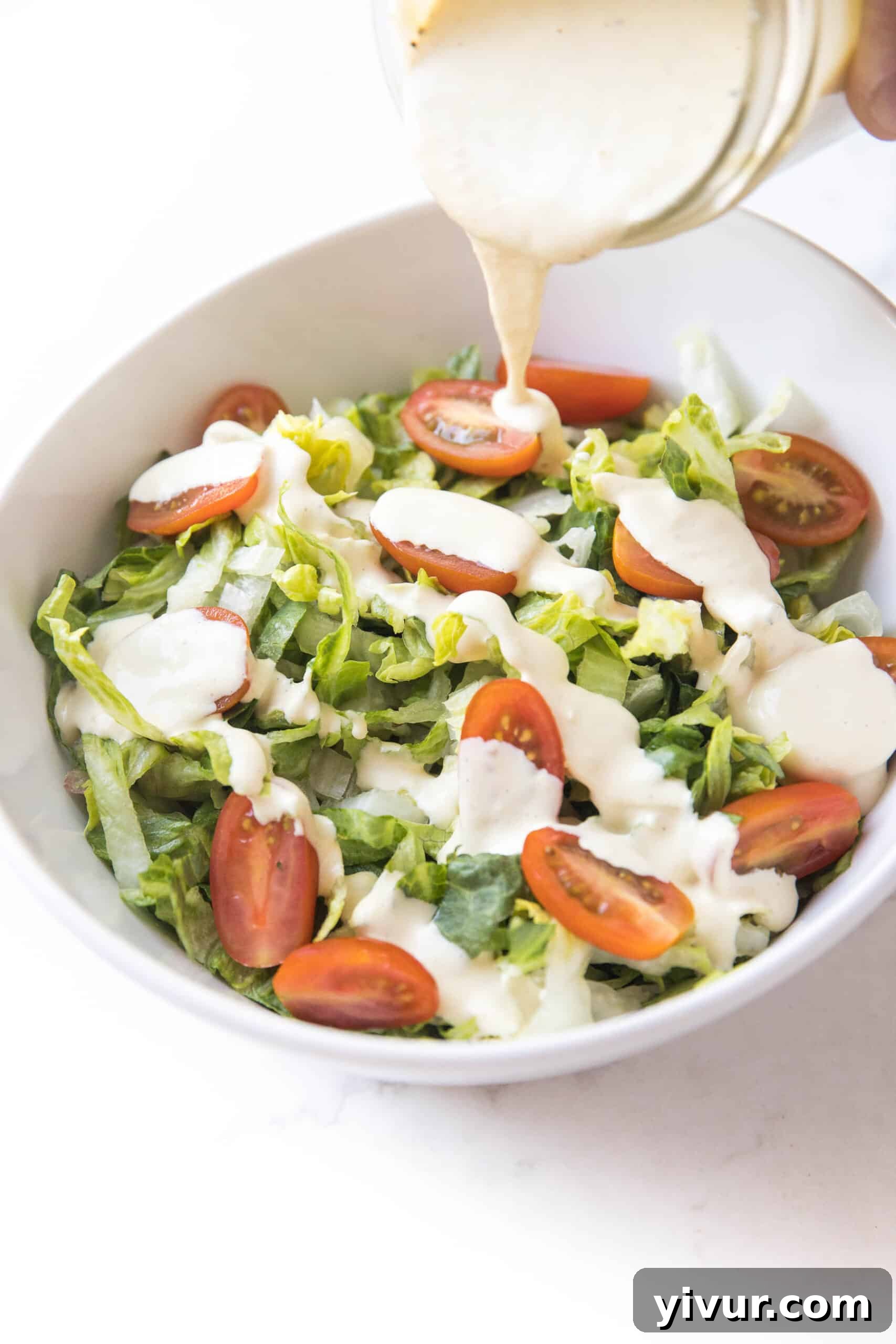 The Ultimate Dairy-Free Keto Caesar Dressing for Whole30 2 Pouring creamy dairy-free keto Caesar dressing over crisp romaine lettuce in a white bowl, ready to be enjoyed as a healthy meal.