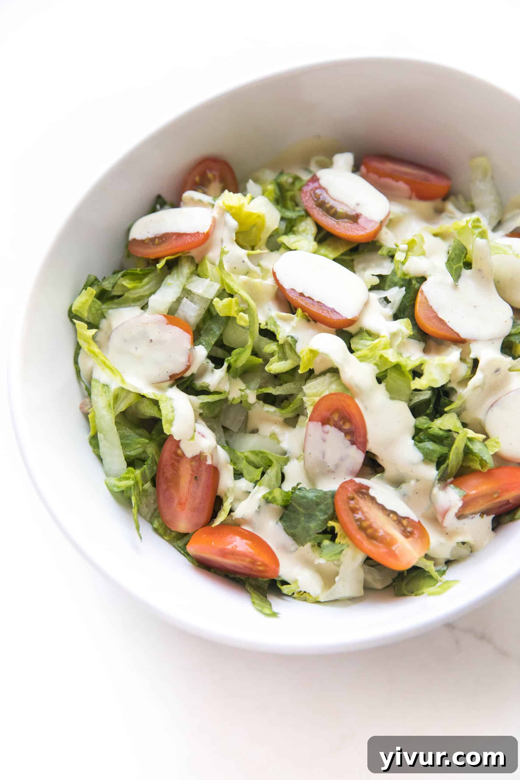 The Ultimate Dairy-Free Keto Caesar Dressing for Whole30 3 Homemade keto Caesar dressing drizzled generously over a fresh salad with vibrant sliced cherry tomatoes and crisp greens, showcasing its creamy texture.