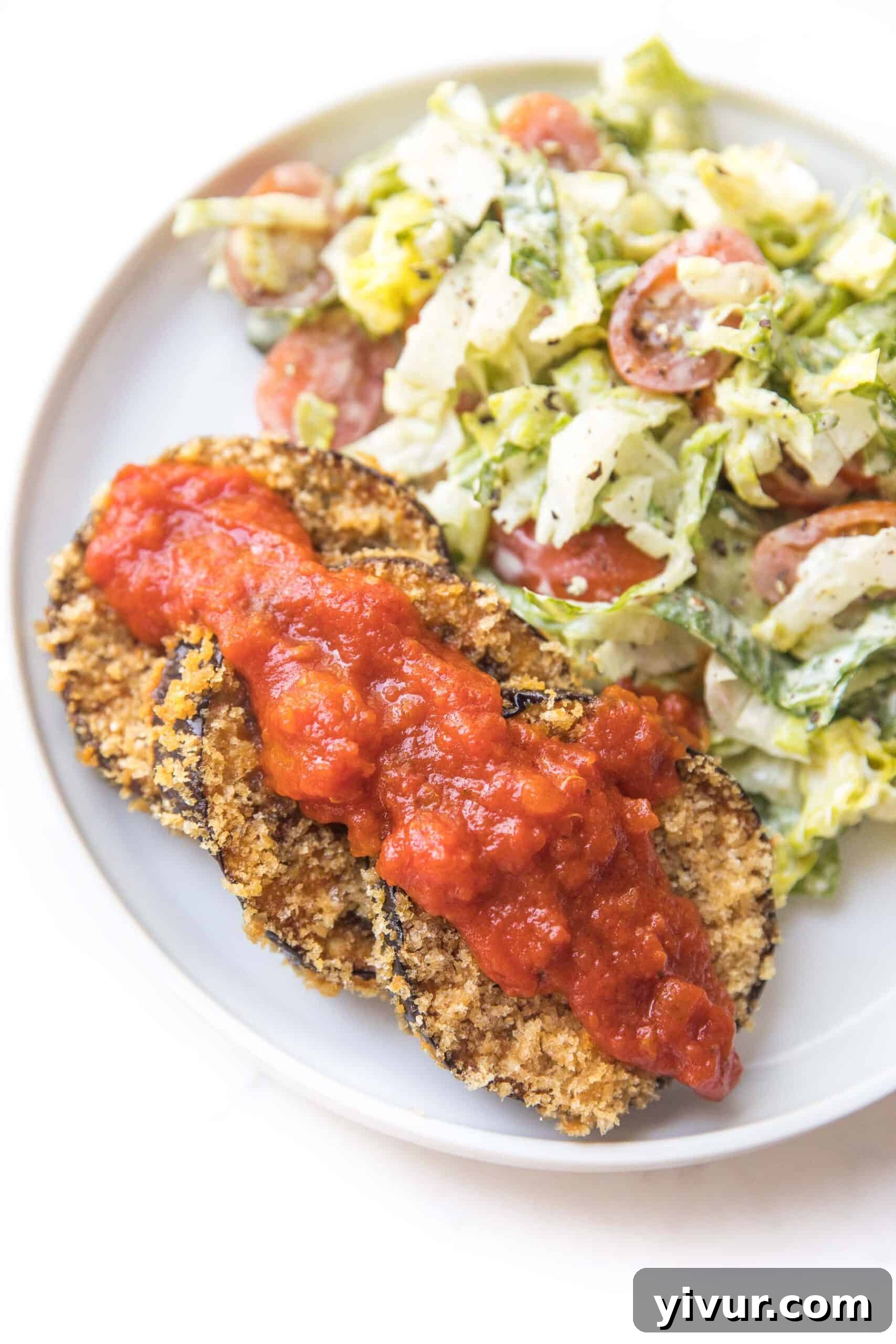 Crispy coated eggplant served alongside a fresh Caesar salad on a pristine white plate