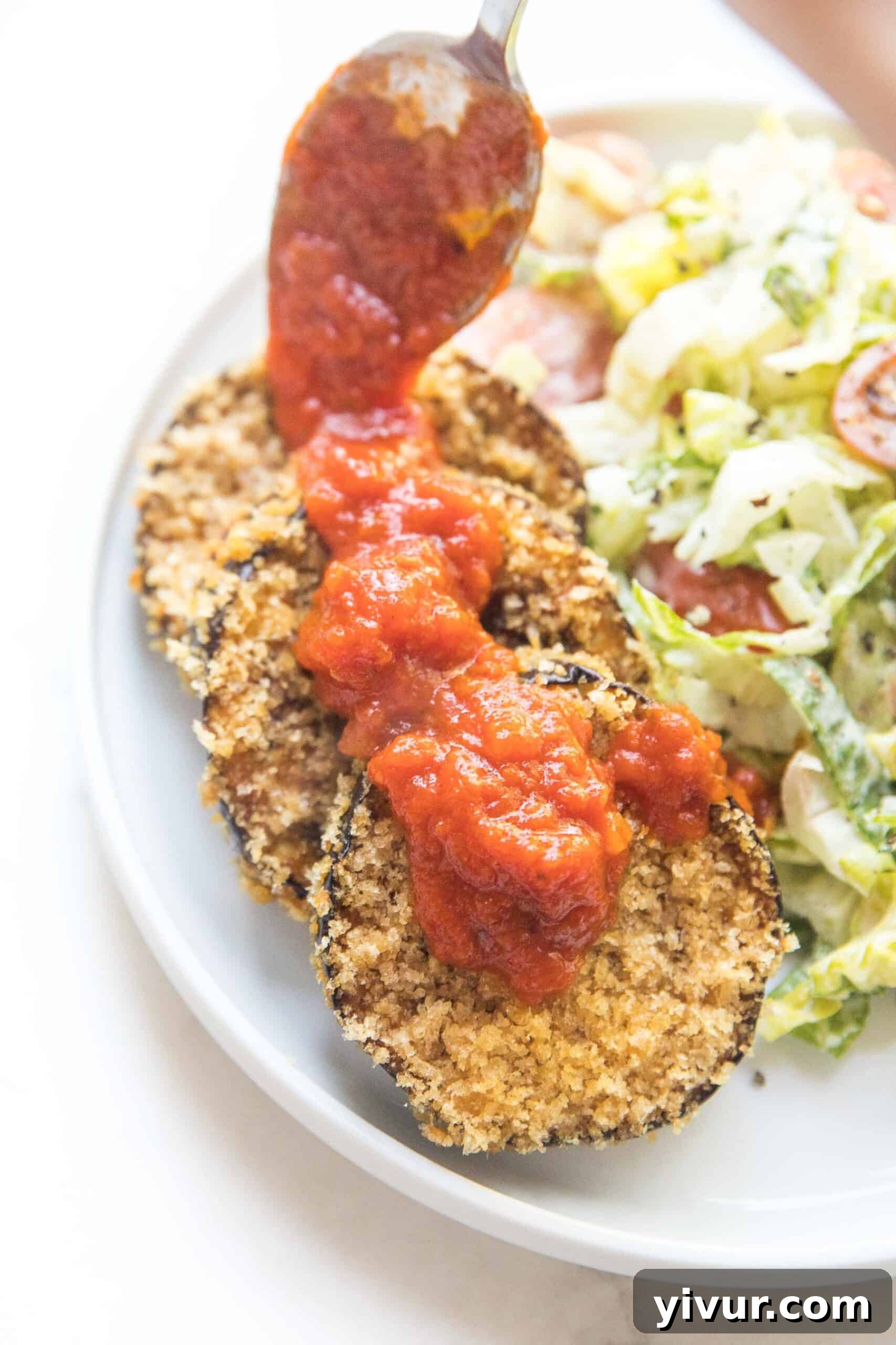Three slices of crispy coated eggplant arranged next to a vibrant Caesar salad on a white plate, ready to be served