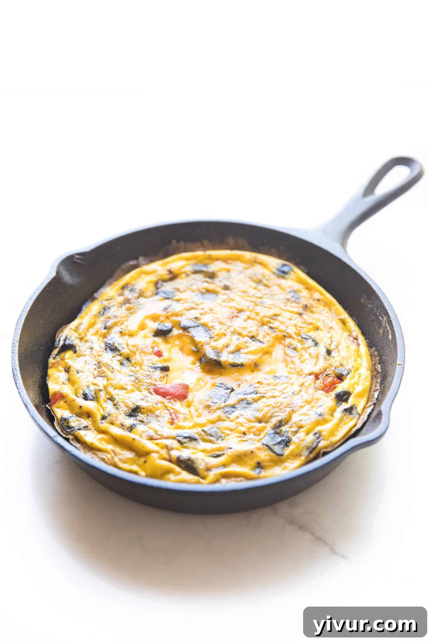 A vibrant keto frittata cooking in a well-seasoned cast iron skillet, set against a clean white background, showcasing its golden-brown edges and colorful vegetable fillings.