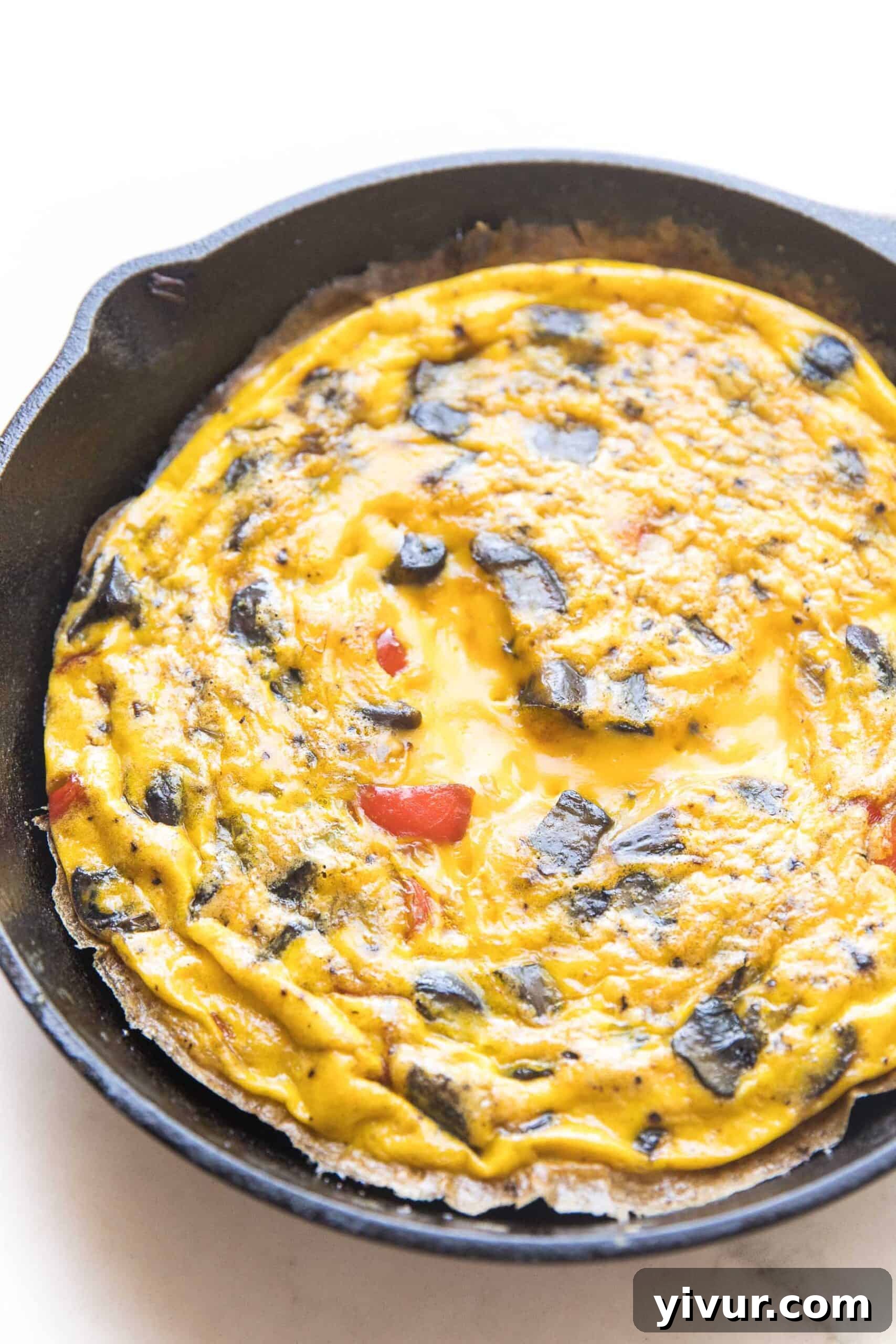 Another view of the perfectly cooked keto frittata, still in its cast iron skillet, showcasing its golden exterior and inviting texture against a bright white background.