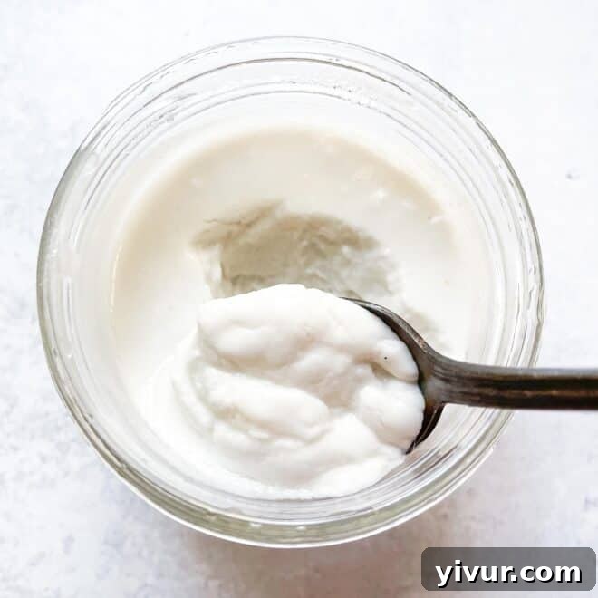 An overhead shot of a small jar of creamy keto coconut yogurt with a silver spoon, perfect for a dairy-free breakfast.