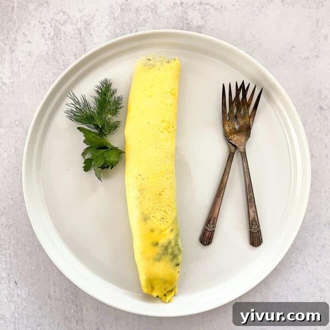 A delicate French omelet presented on a white plate, garnished with fresh dill and parsley, accompanied by two antique forks.