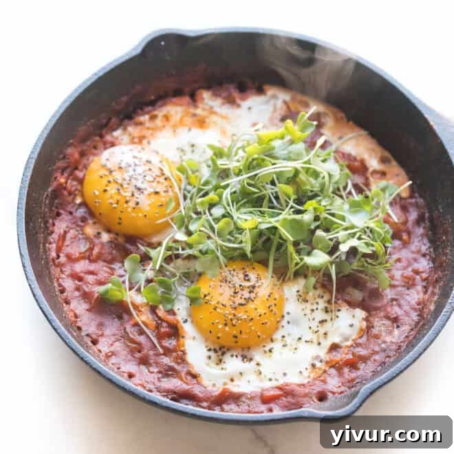 A hearty bowl of Keto Shakshuka, with eggs gently poached in a rich and spicy tomato sauce, garnished with fresh herbs.