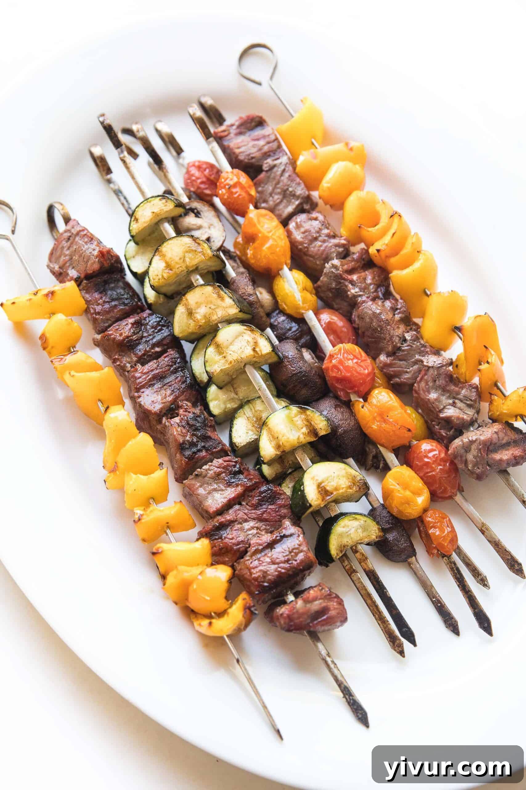 Grilled steak and vegetable kabob skewers on a white platter, perfectly cooked and ready to serve